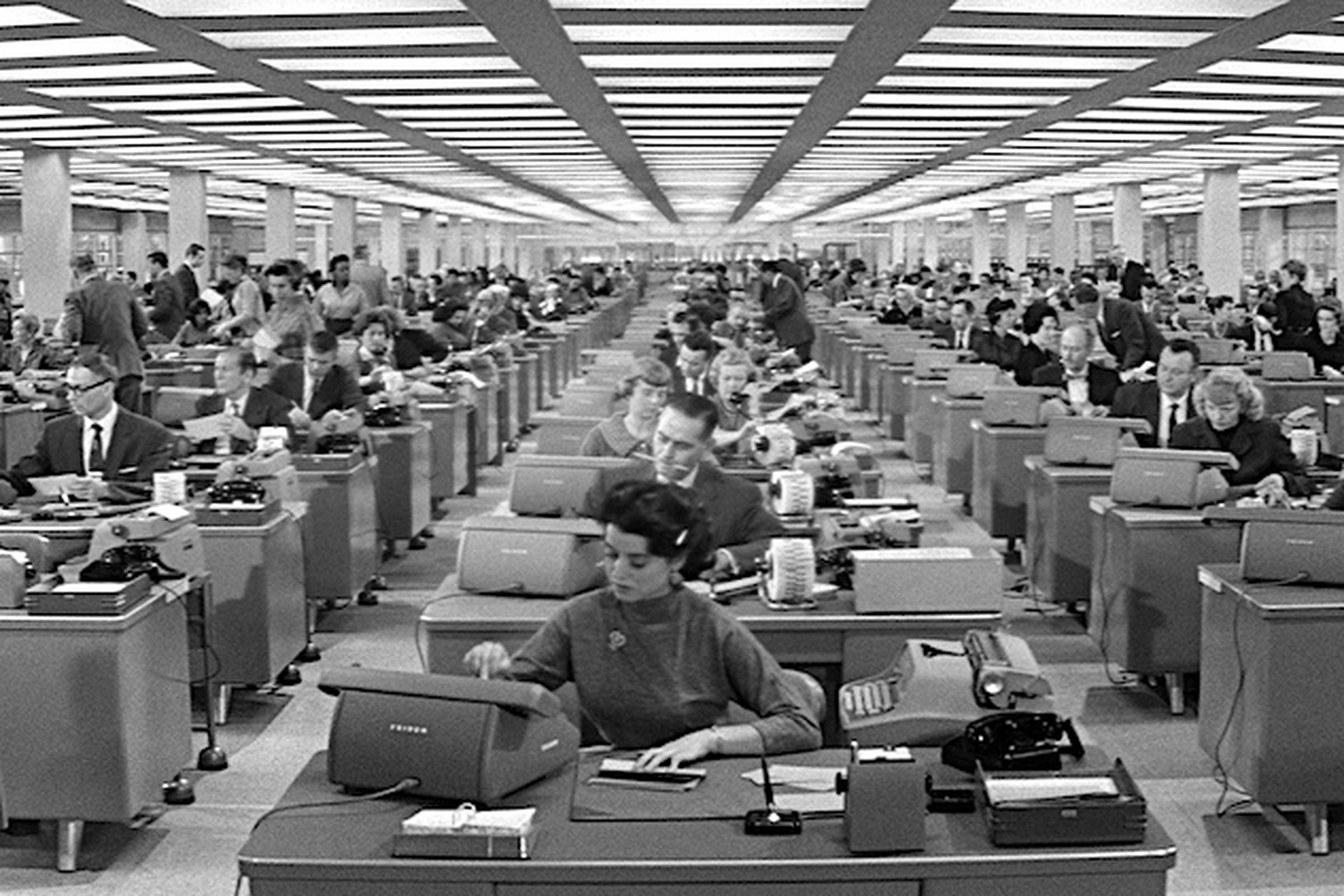 A 1960s-style open office, with rows of desks and people working.