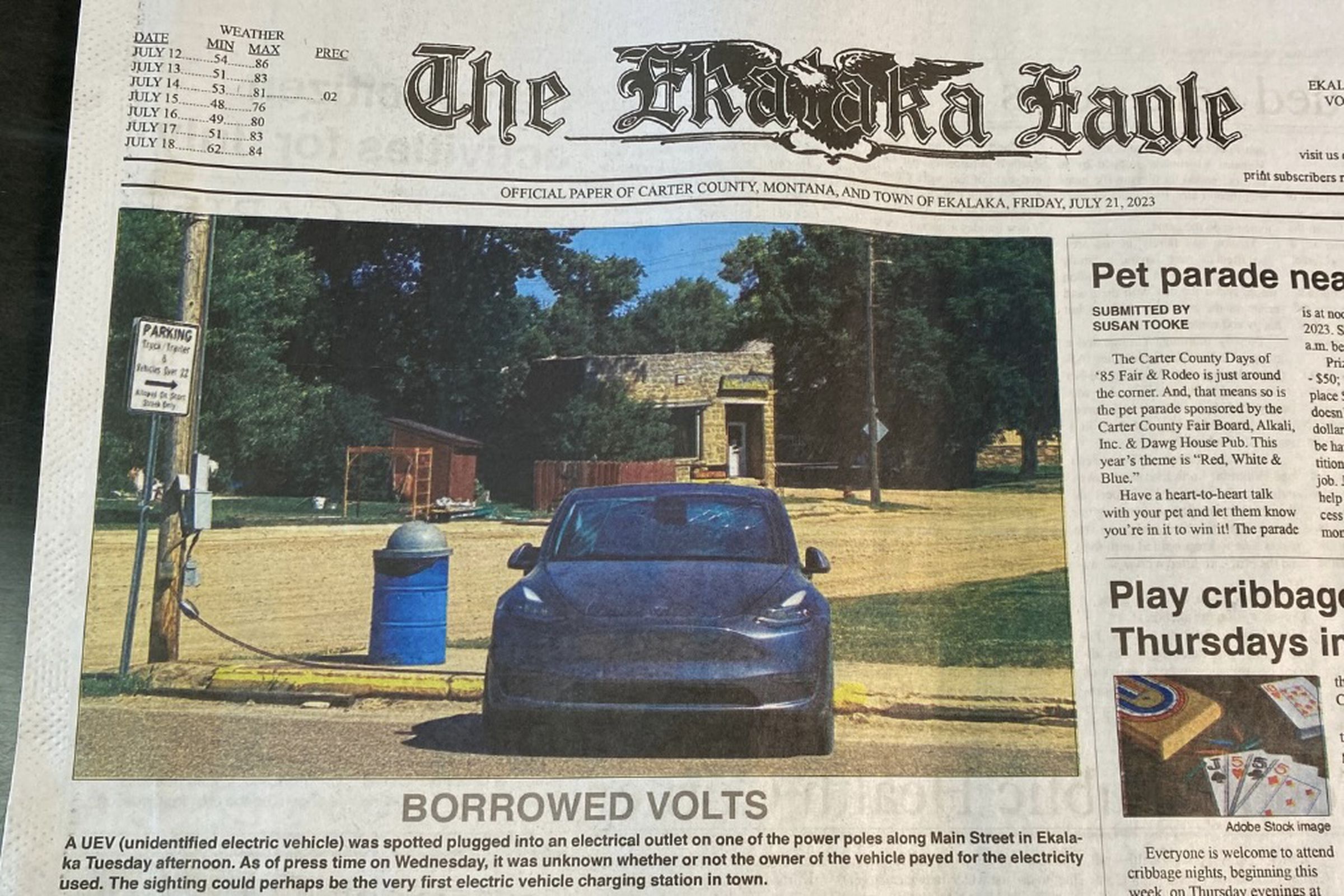 Newspaper front page shows black Tesla model Y on a small main street plugged into a pole