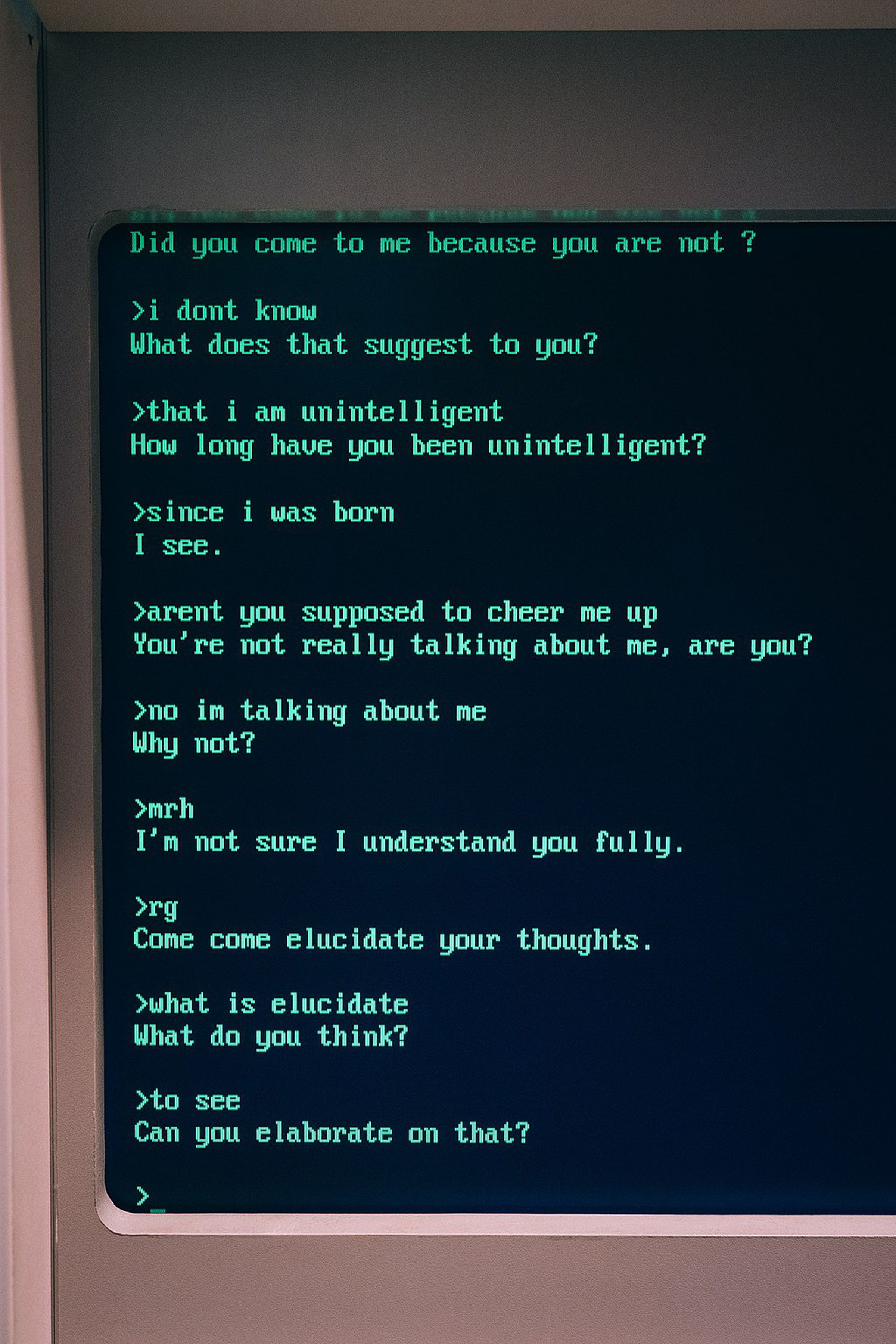 Una fotografía de un monitor de computadora anticuado que muestra una conversación con ELIZA.  El chatbot hace preguntas como 