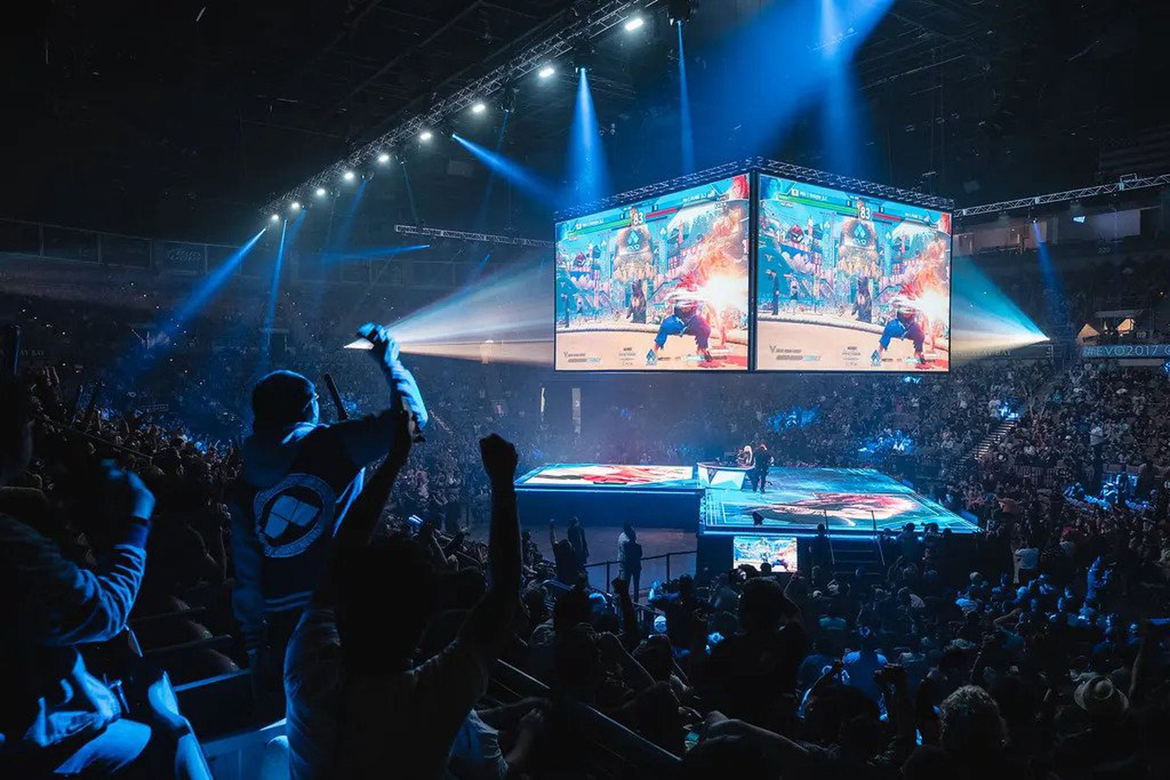 Photo from the EVO tournament that shows a darkened stadium filled with fans cheering as a Street Fighter V match plays on the main stage.