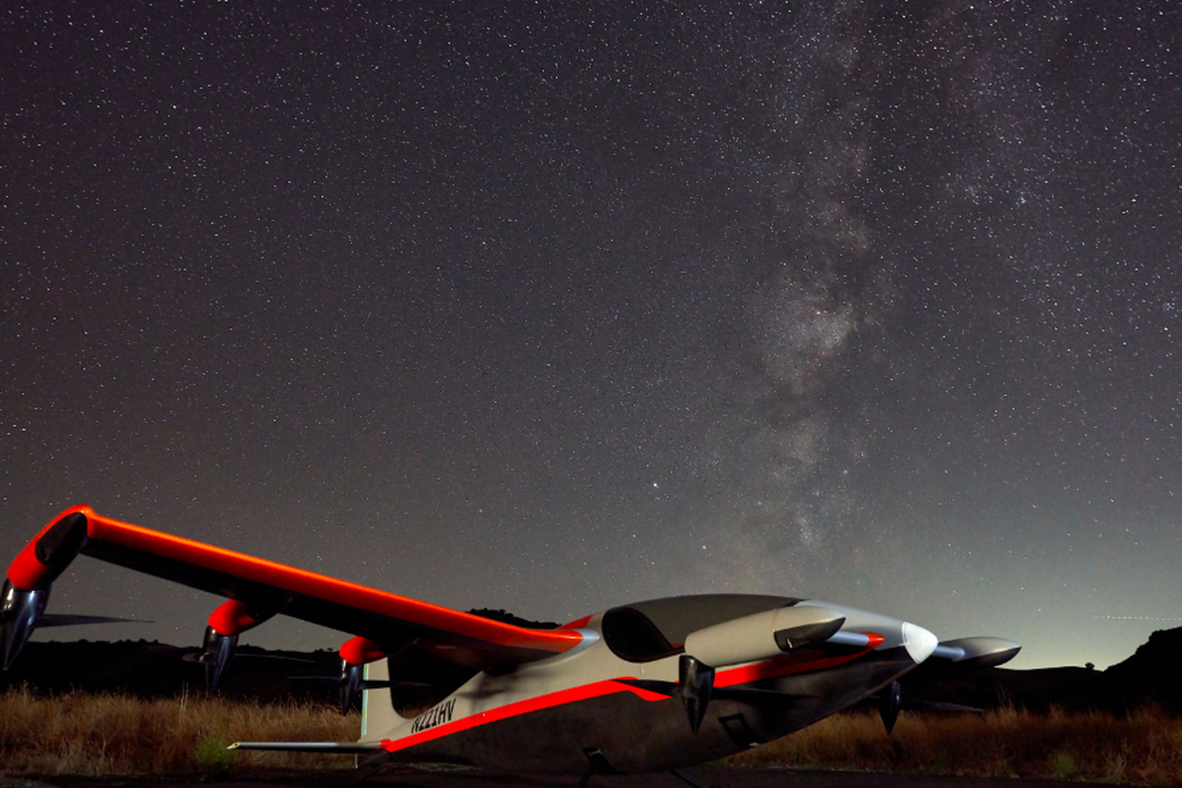 In a clear and starry night sky, a red charter-sized aircraft stands.