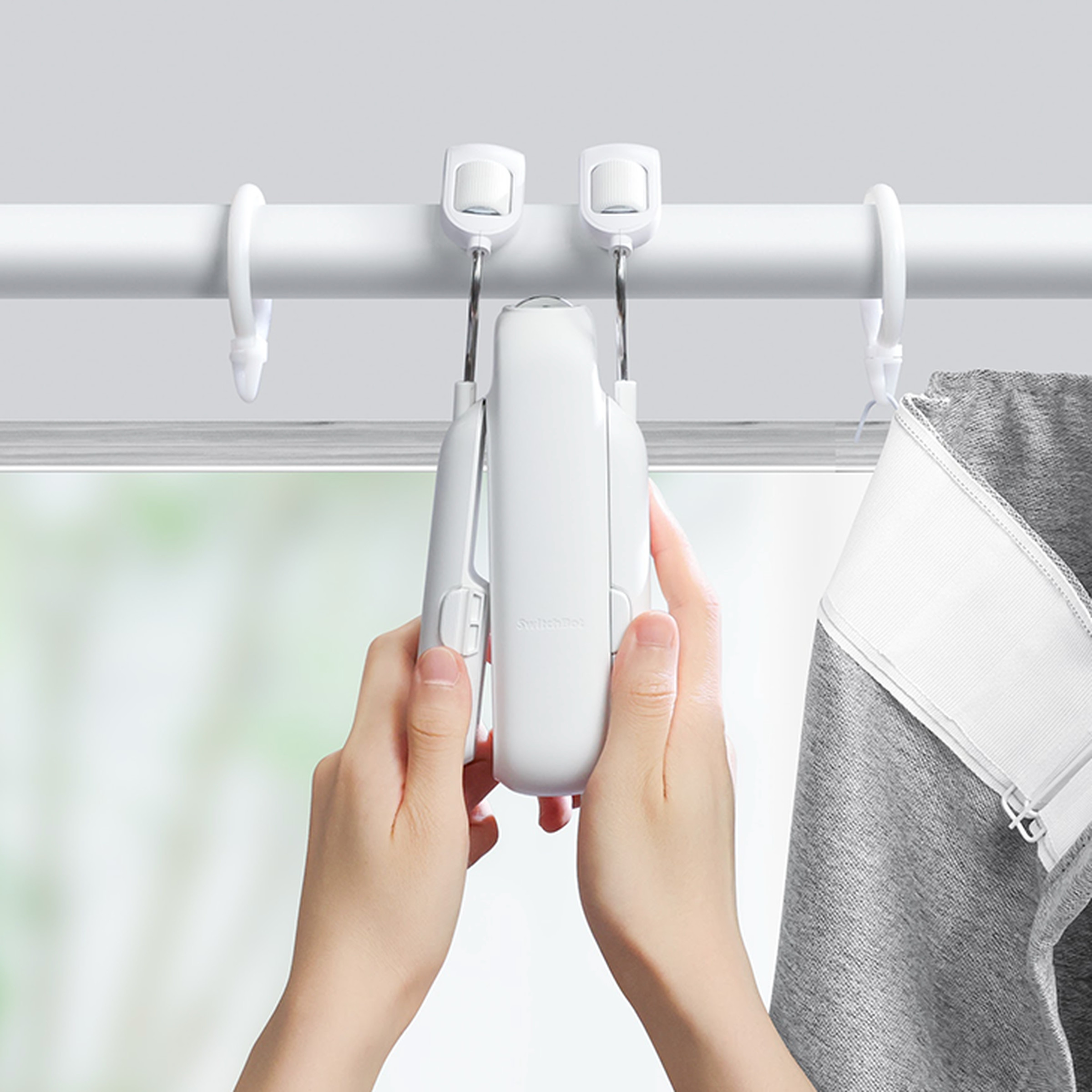 A picture of a person’s hands installing the SwitchBot 3 on a telescoping curtain rod.