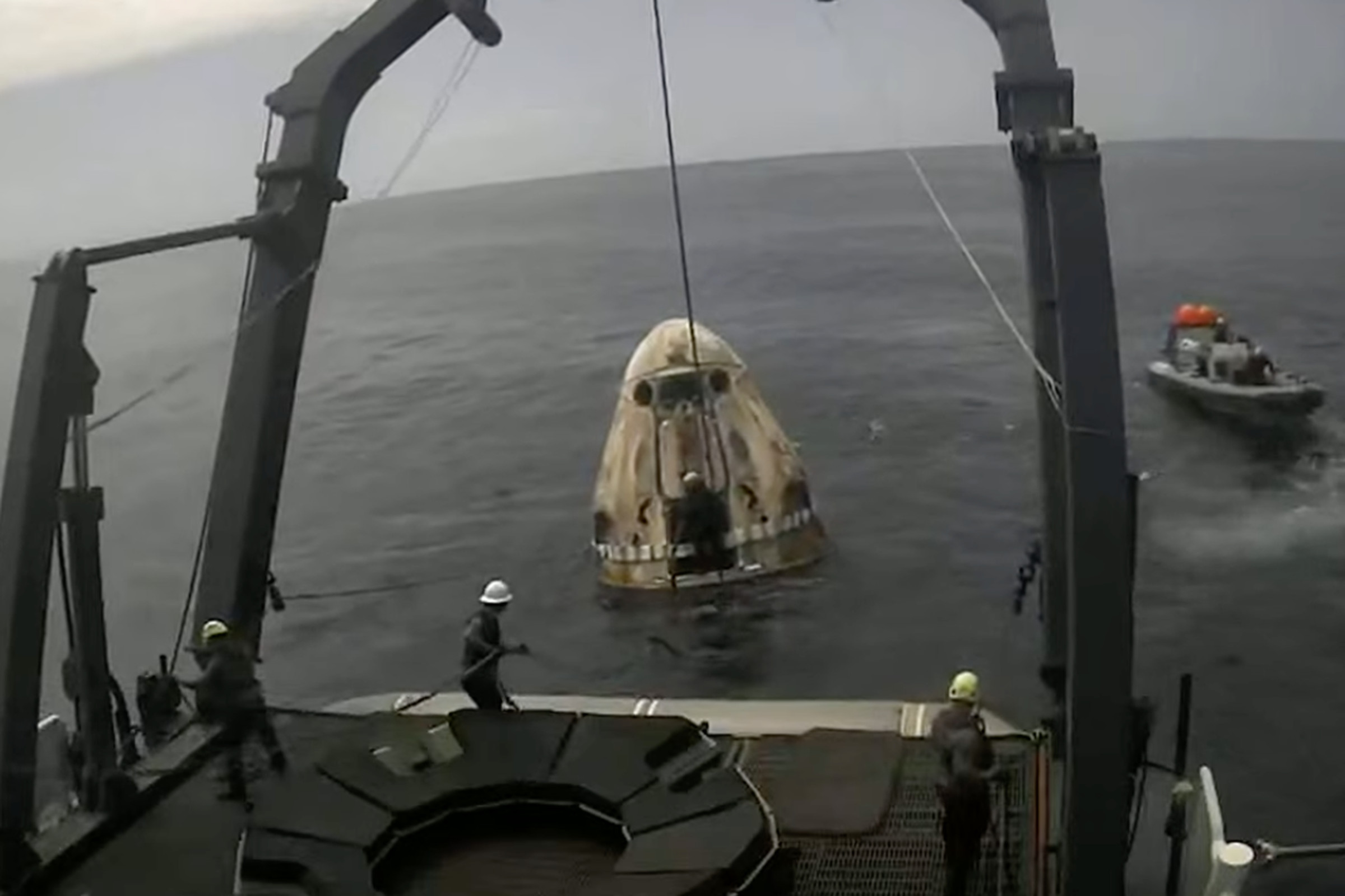A crew dragon capsule bobs in the water, connected to a larger boat with tethers