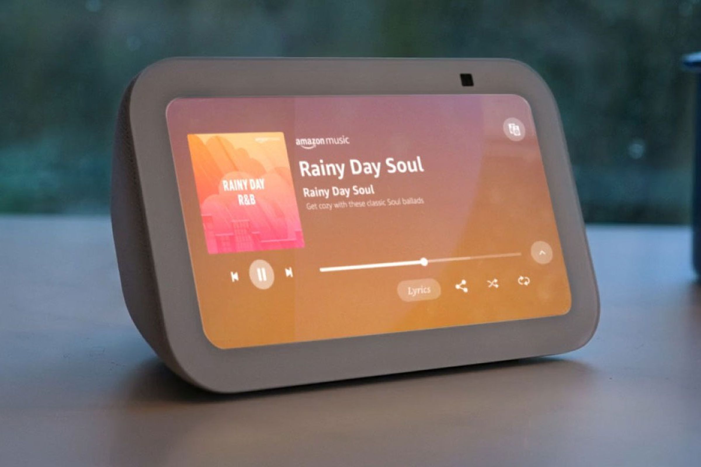 The third-gen Echo Show 5 turned on while on a desk in front of the window during a rainy day.