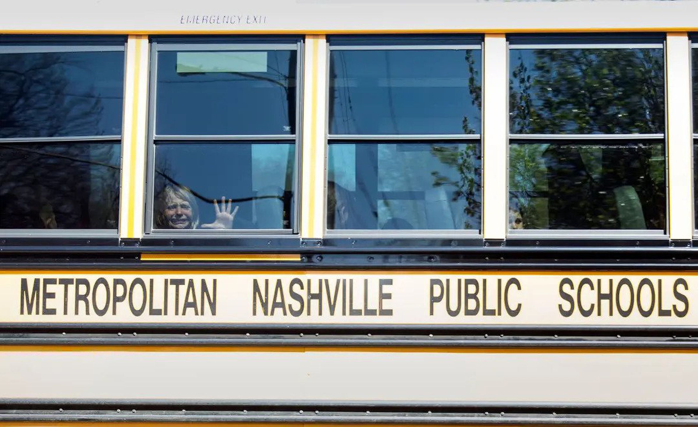 A schoolbus with a crying child placing their hand against the window.