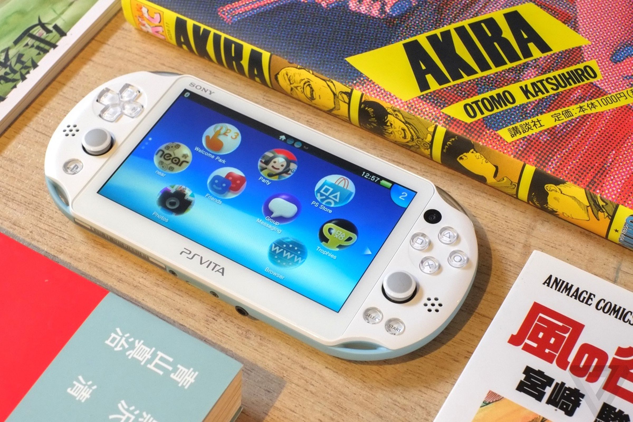 The PS Vita sitting on a table, nested between an Akira manga and several other books.