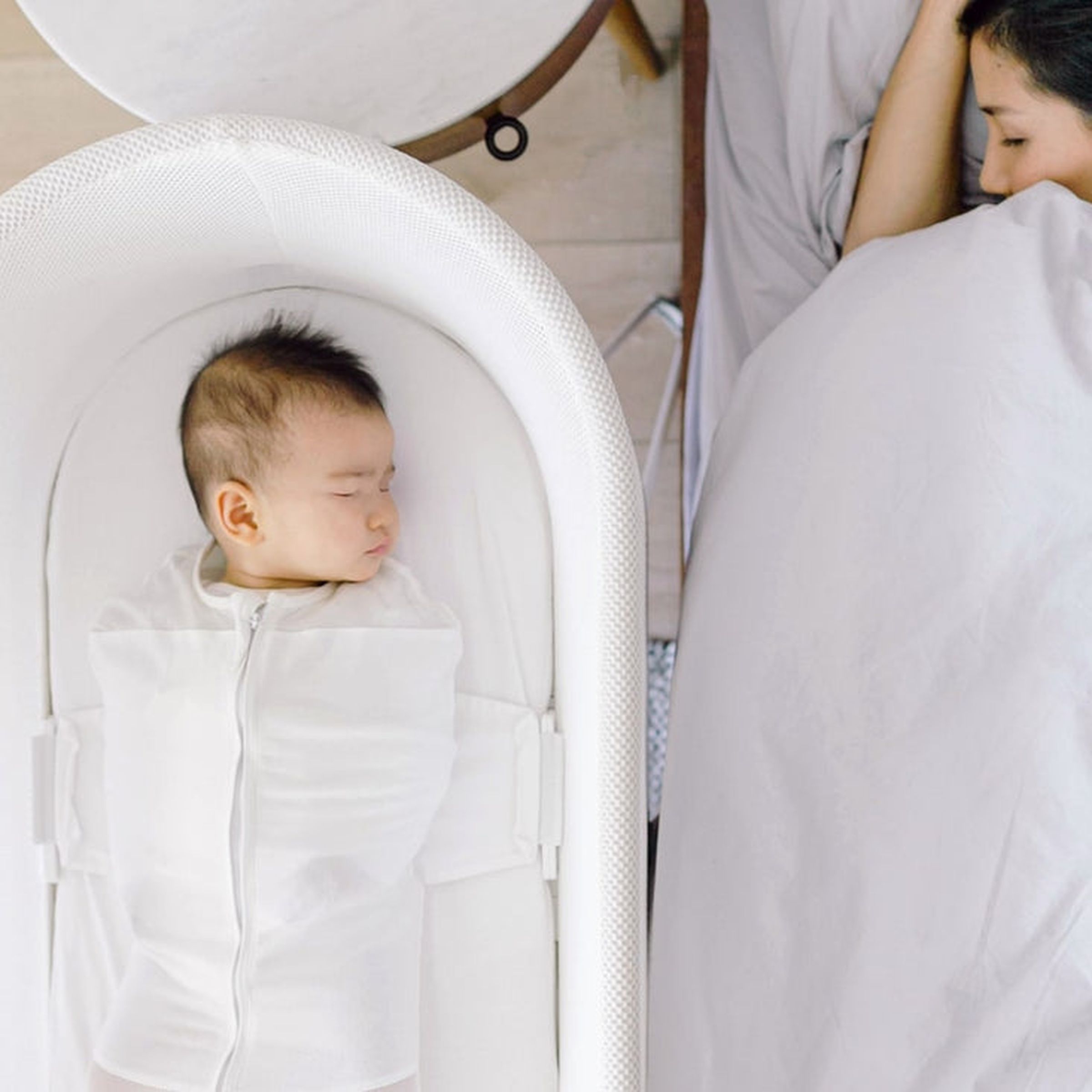 A photo of a baby sleeping a Snoo bassinet next to a person in a bed.