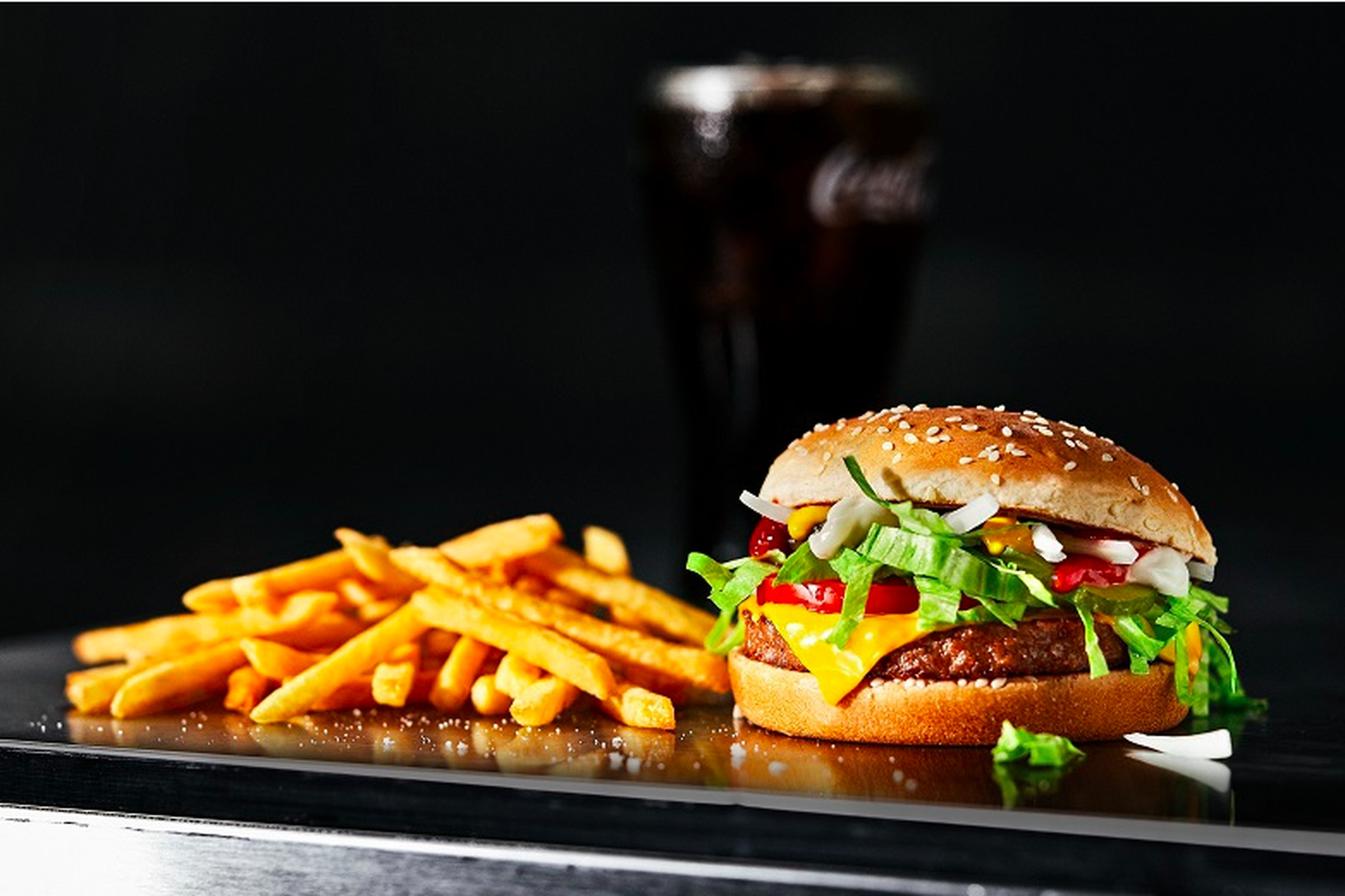 A photo of a burger, french fries, and a soda in front of a black background.