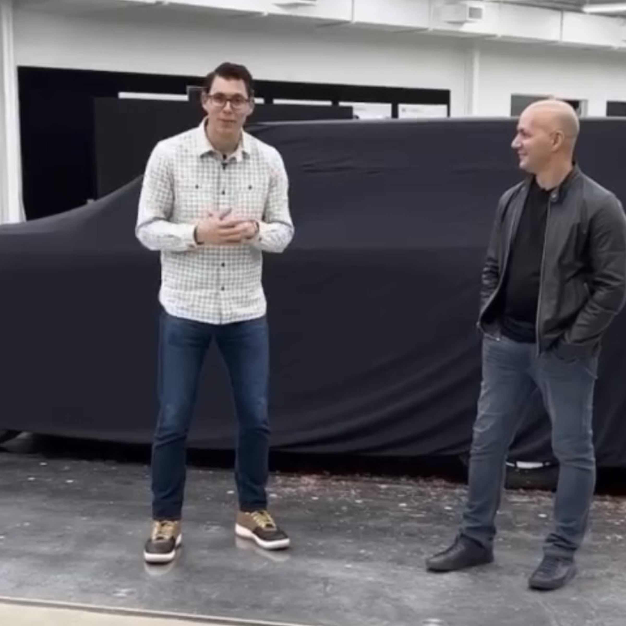 Black cloth covering a clay model of the R2 SUV with CEO RJ Scaringe and lead designer Jeff Hammoud standing in front of it.