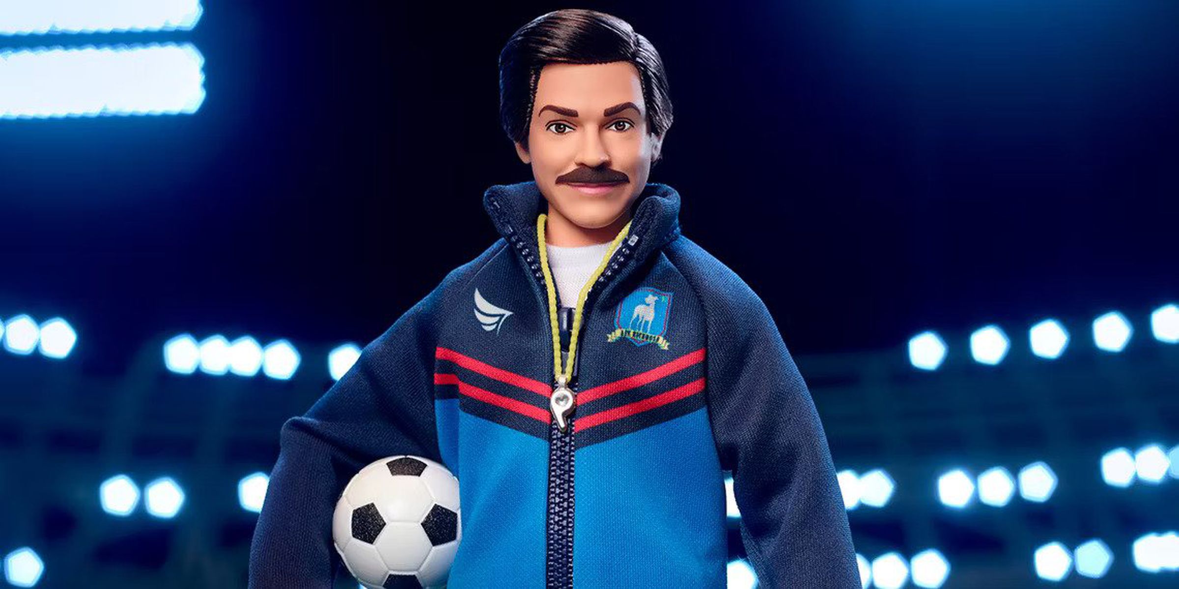 Image of the Ted Lasso Barbie featuring actor Jason Sudeikis as his character soccer coach Ted Lasso wearing a blue jacket and holding a soccer ball.