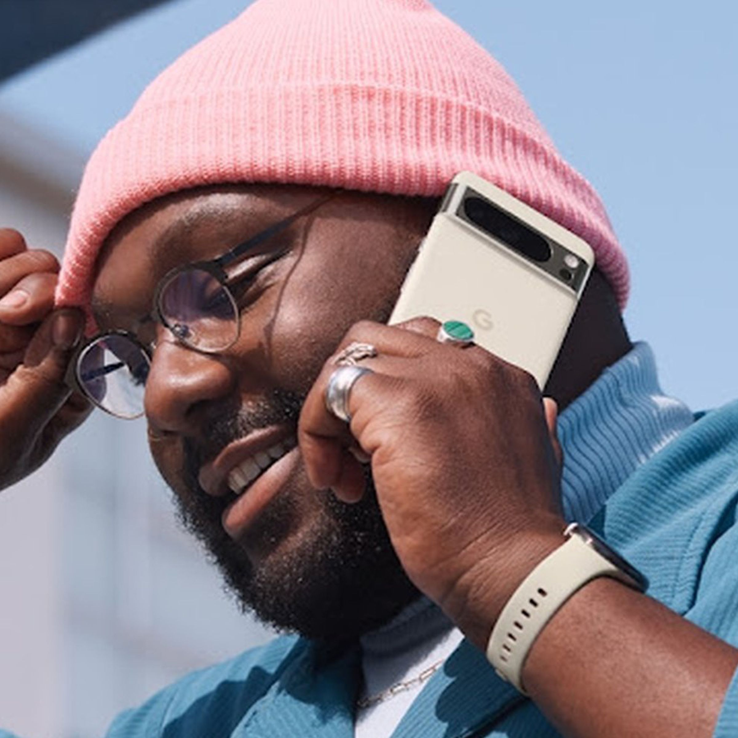 A man in glasses and a knit cap talks on a cellular phone, described by Google as the Pixel 8 Pro in porcelain.