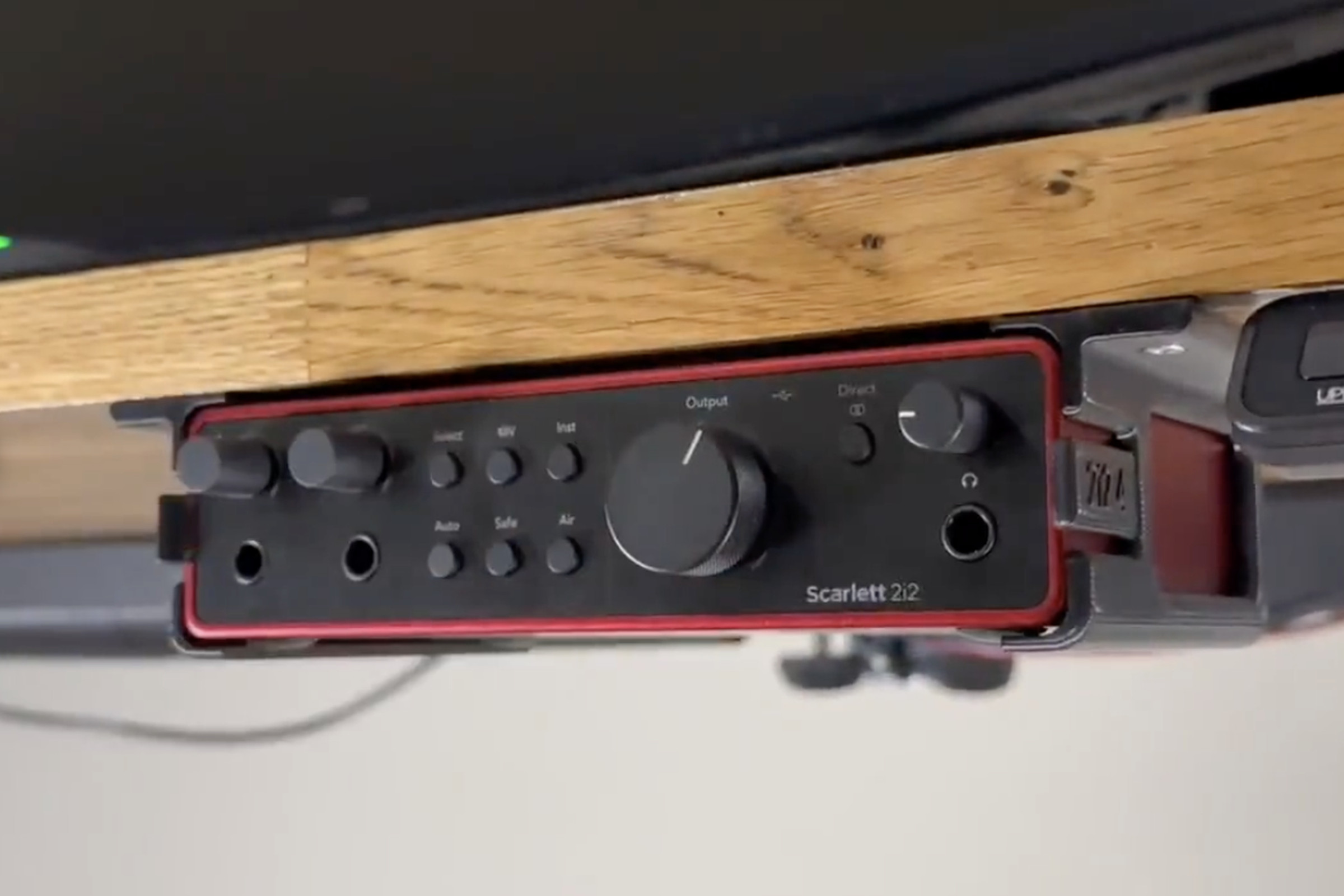 Red audio interface device in a bracket under a desk.