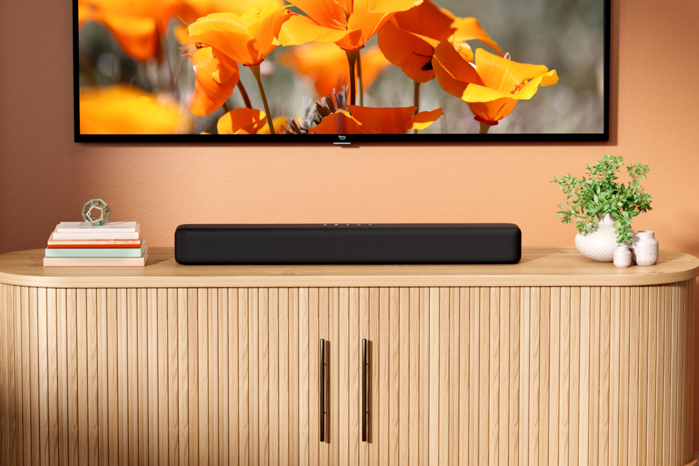 The Amazon Fire TV Soundbar positioned under a TV, sitting on a piece of furniture.