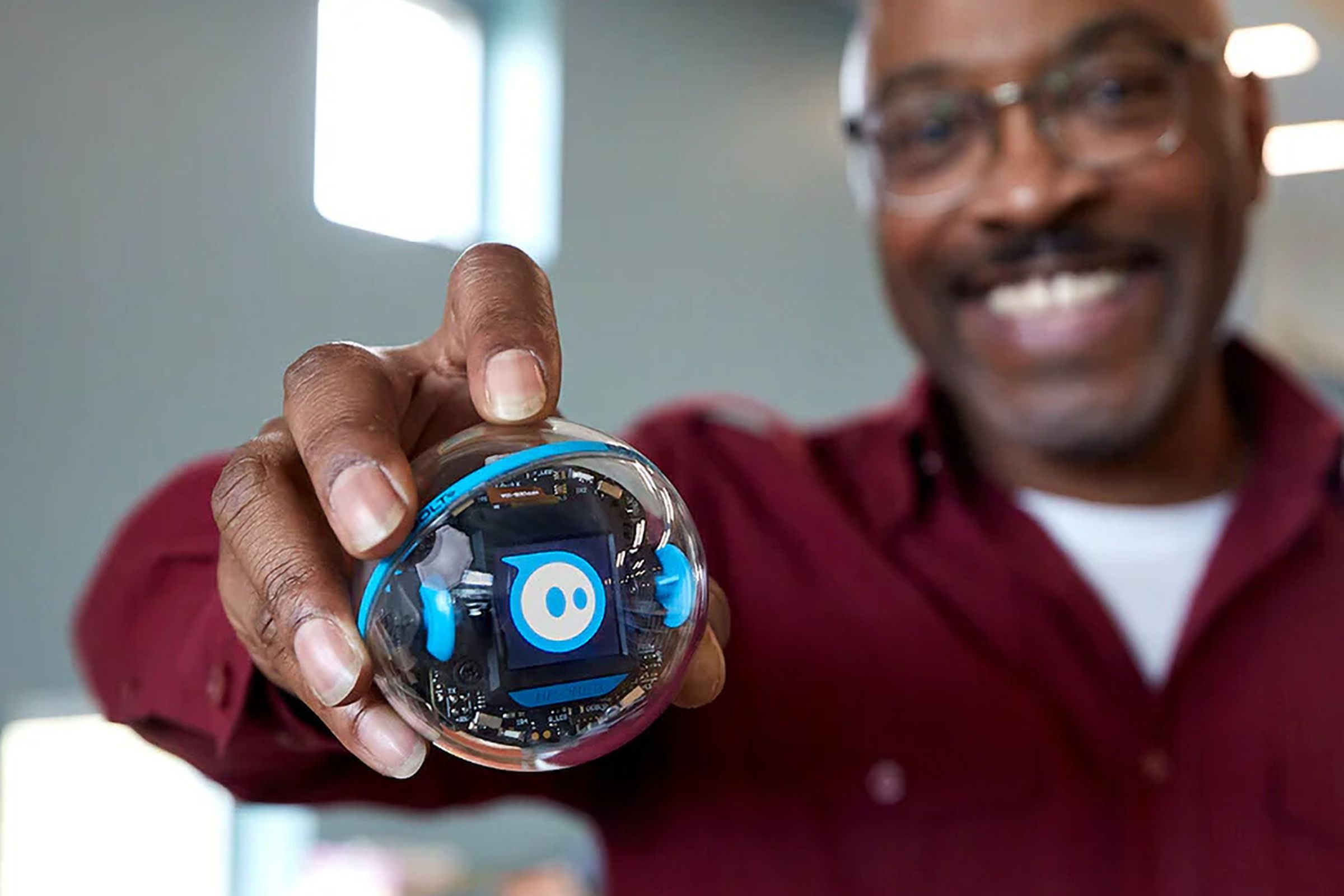 A teacher holds the Sphero Bolt Plus robot in their hand out toward the camera.