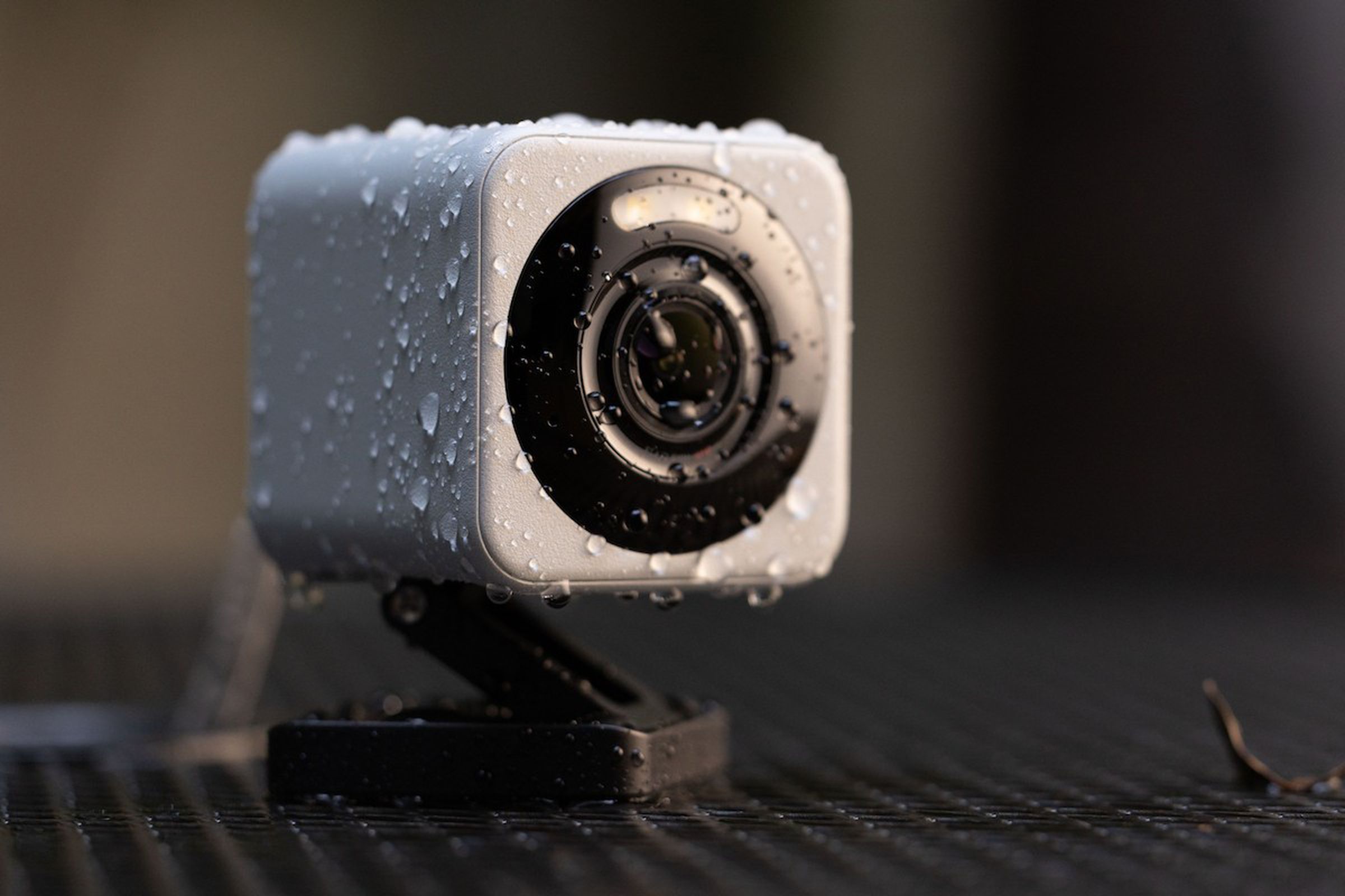 closeup of a small cube camera with a z-shaped folding stand, covered in little water droplets, on a park table next to a leaf