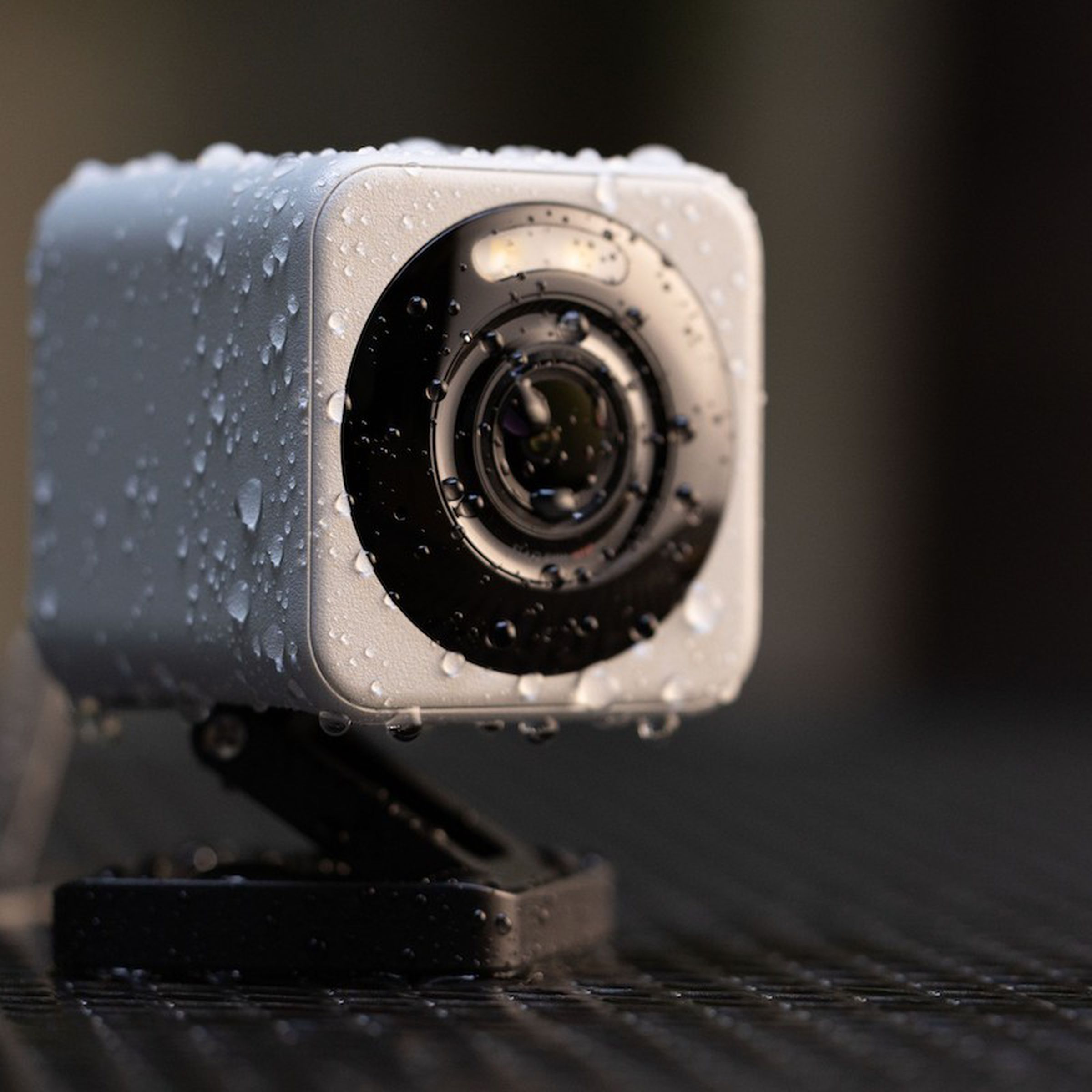 closeup of a small cube camera with a z-shaped folding stand, covered in little water droplets, on a park table next to a leaf
