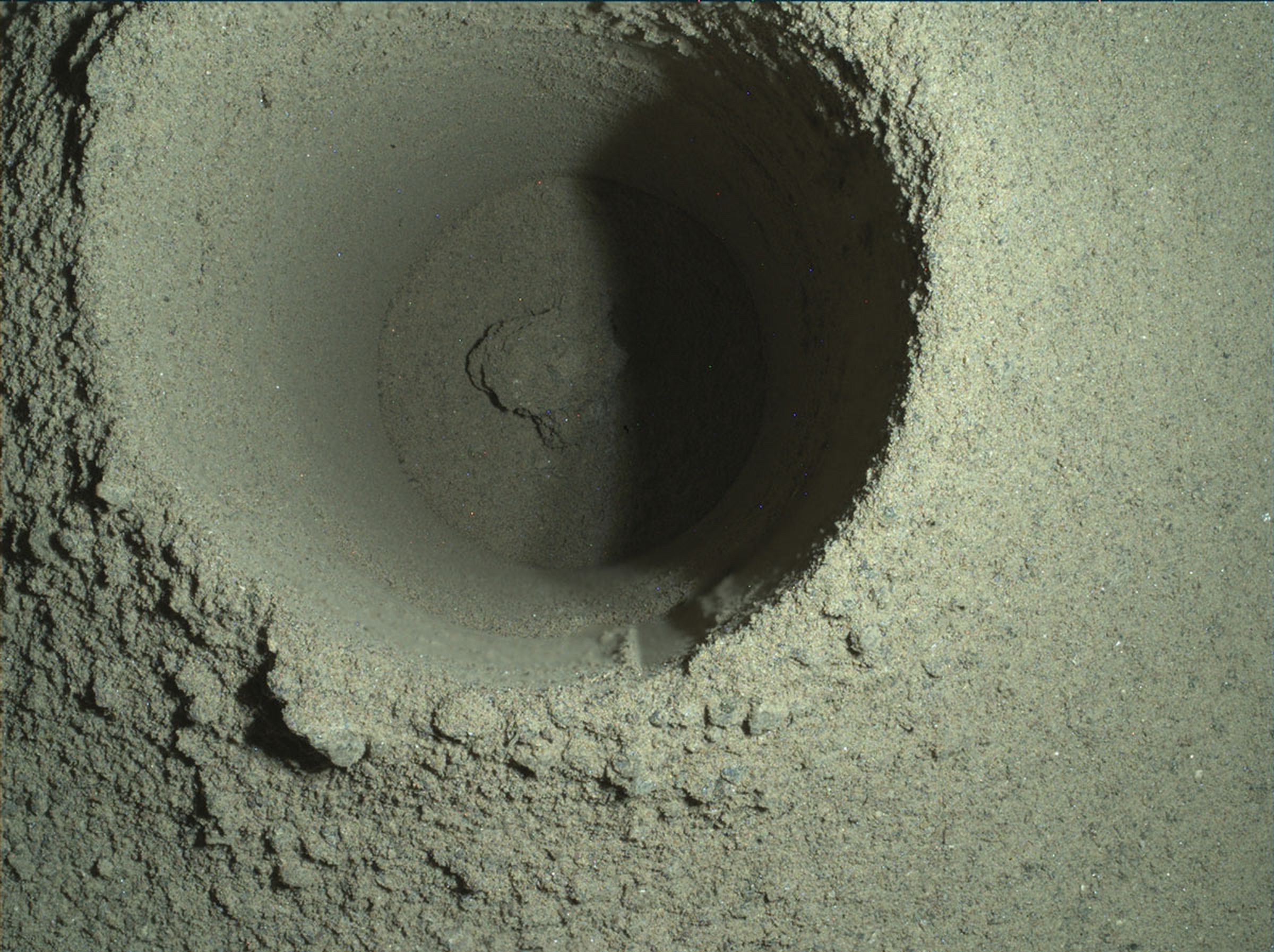 A closeup image of the borehole drilled by Perseverance, showing a mound of dusty material that scientists suspect slipped out of the rover’s drill bit tube.