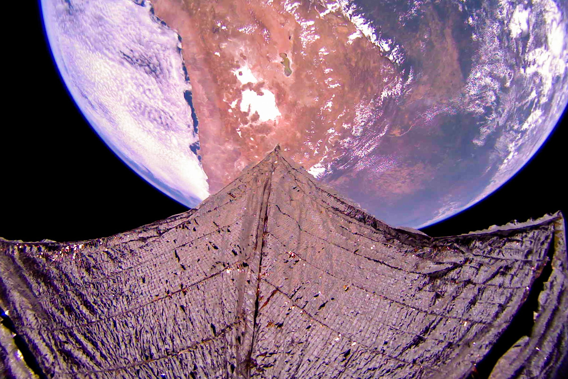 A metallic solar sail fills the bottom of the image. Above it part of the disc of the Earth is visible, with part of South America dominating the view.