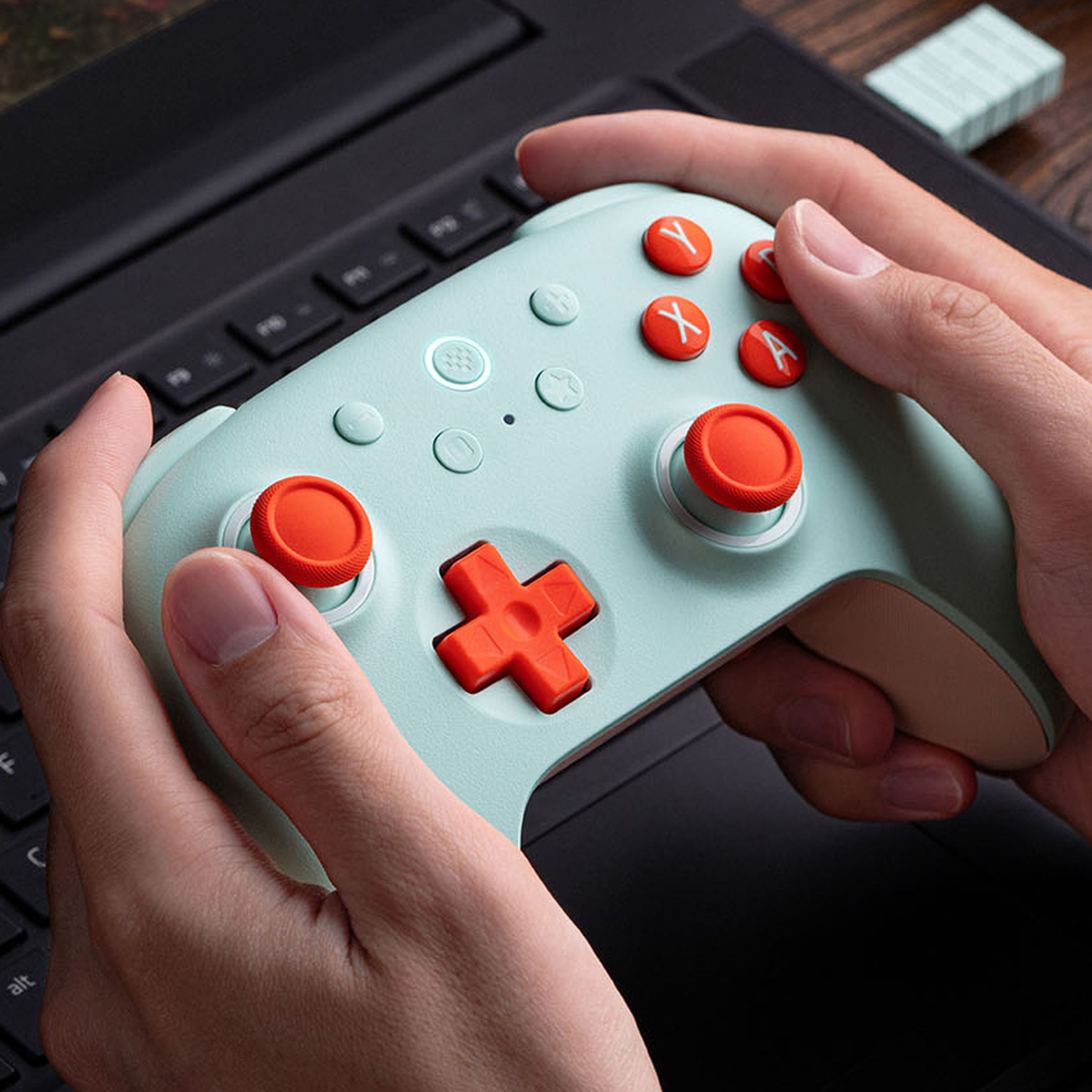 A gamer holding the 8BitDo Ultimate 2C Wireless Controller in front of a laptop computer.