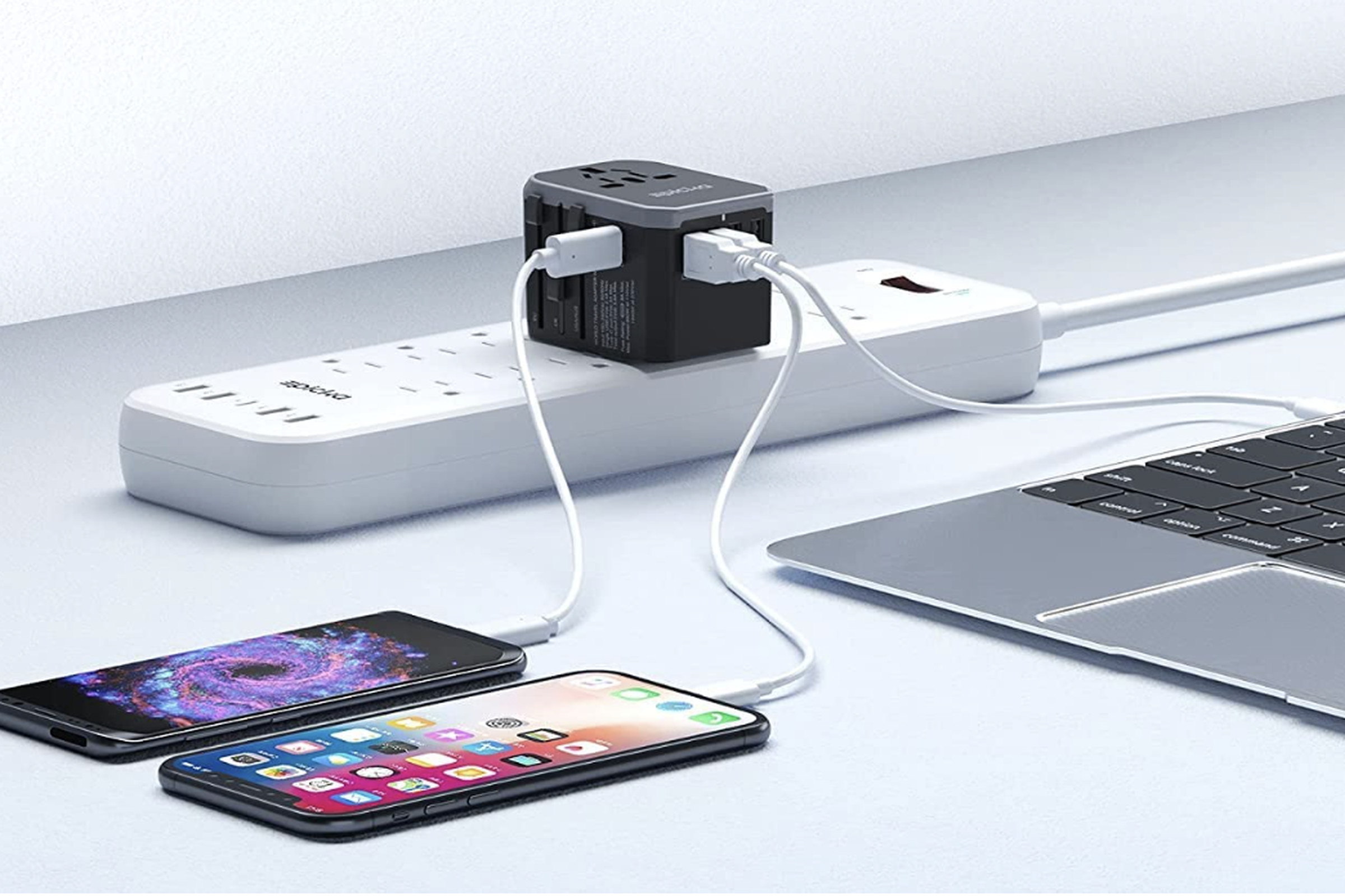 Travel adaptor on power strip connected to phones and laptop.