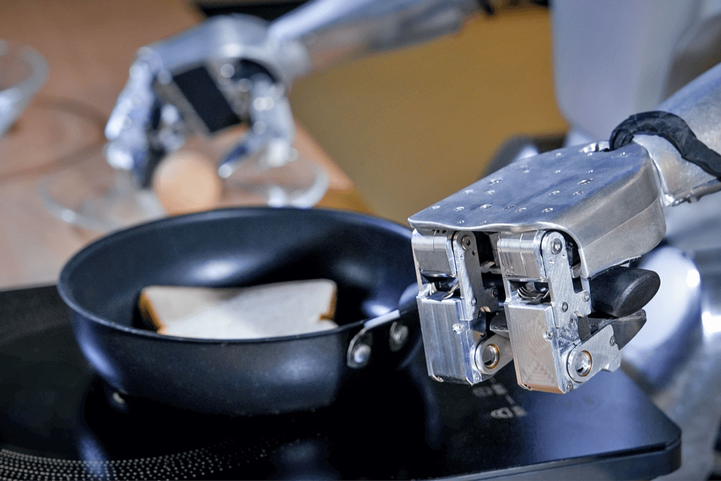 A close-up of Unitree’s G1 humanoid robot’s three-fingered hand grasping the handle of a frying pan.