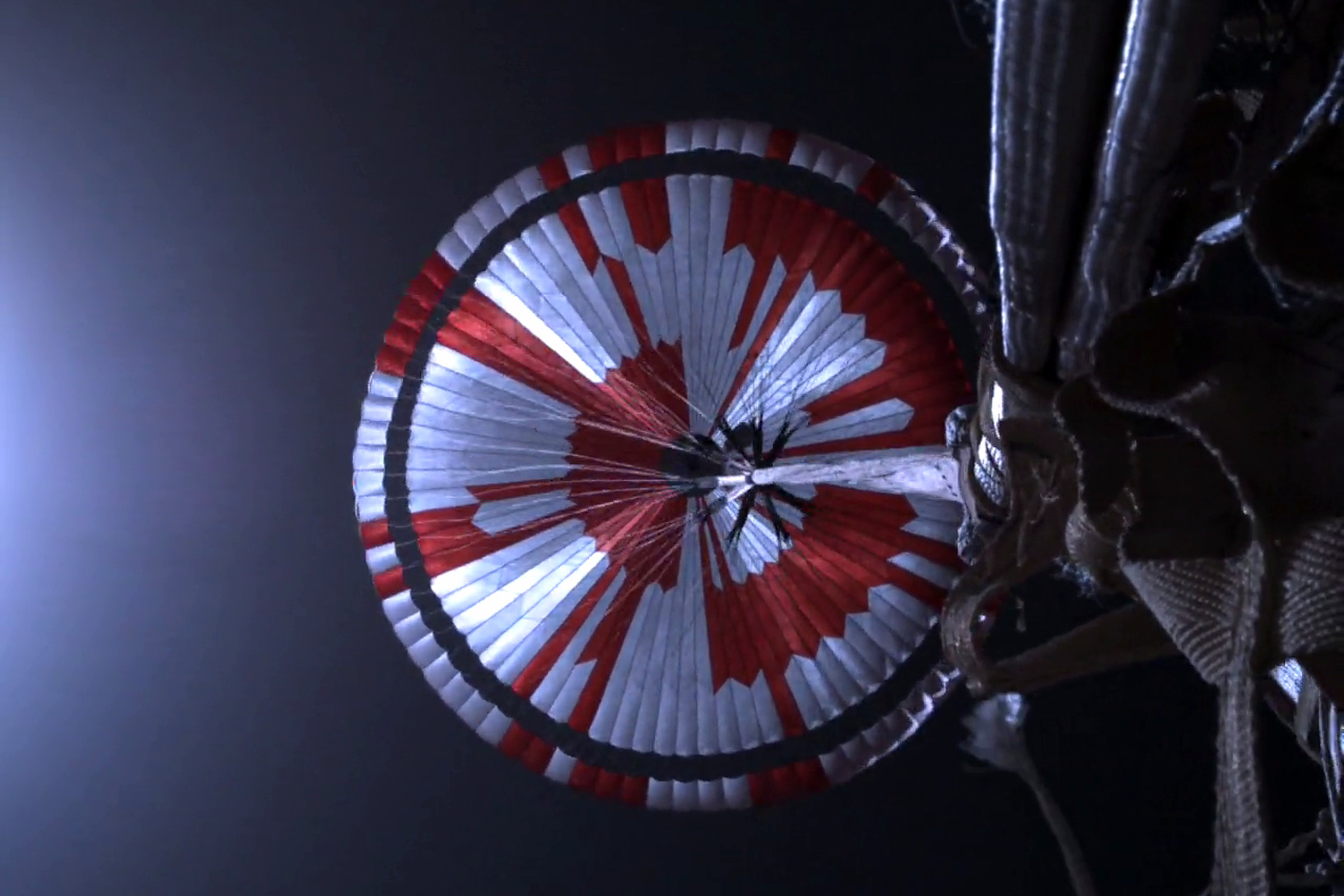 The view of NASA’s Perseverance rover looking up at its parachute, which reads “Dare Mighty Things” in a hidden code, while zooming through the Martian atmosphere before landing.