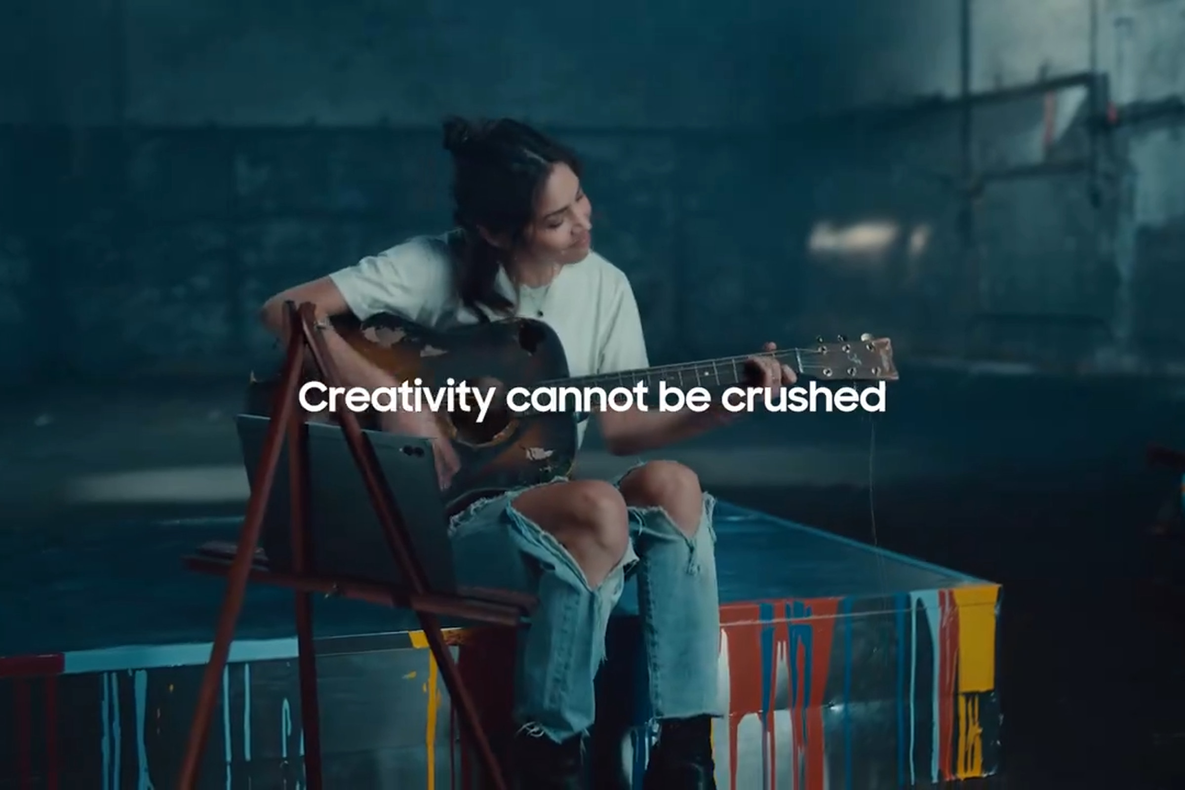 Still image from Samsung “Uncrush” video showing a woman in ripped jeans playing a guitar and the message “Creativity cannot be crushed.”