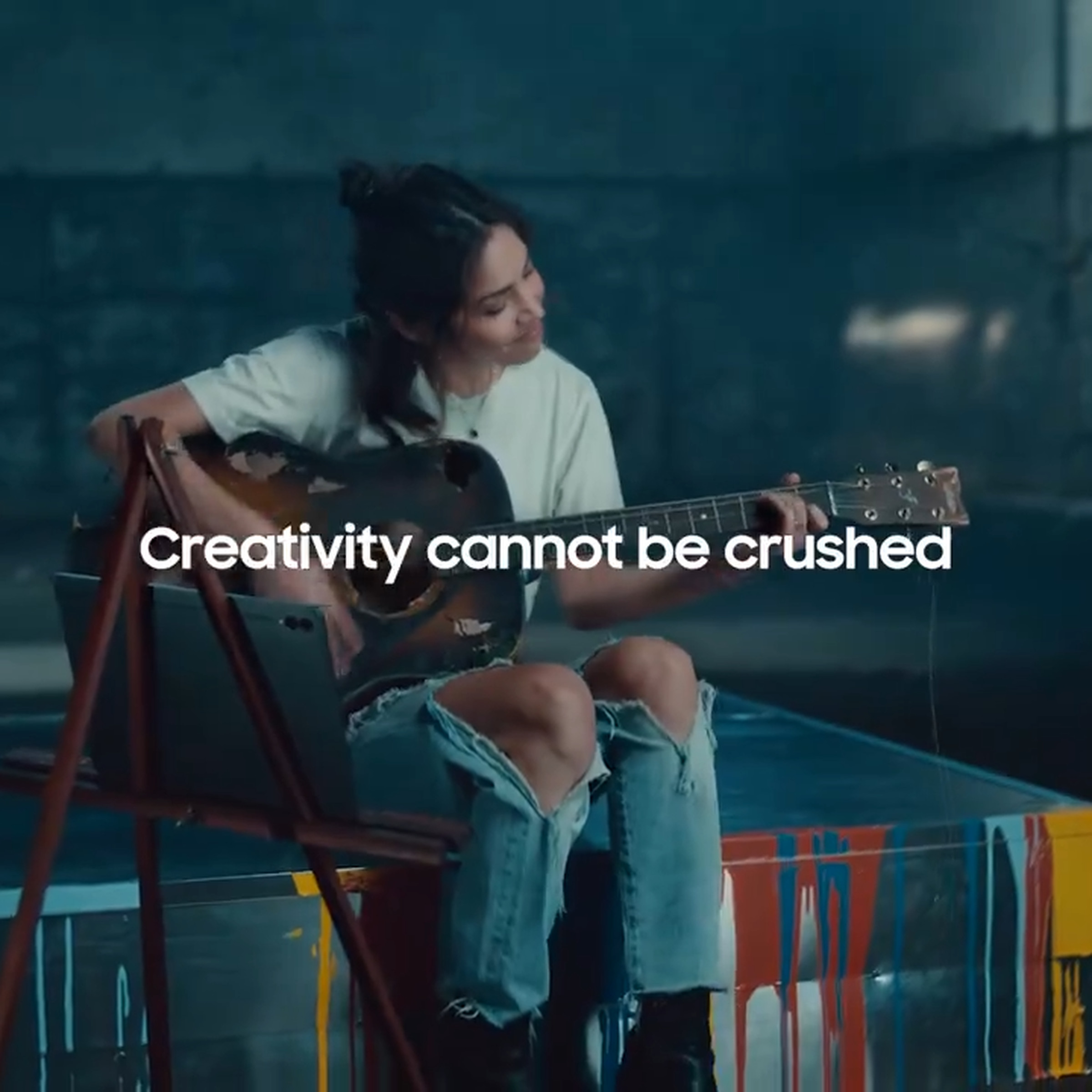 Still image from Samsung “Uncrush” video showing a woman in ripped jeans playing a guitar and the message “Creativity cannot be crushed.”