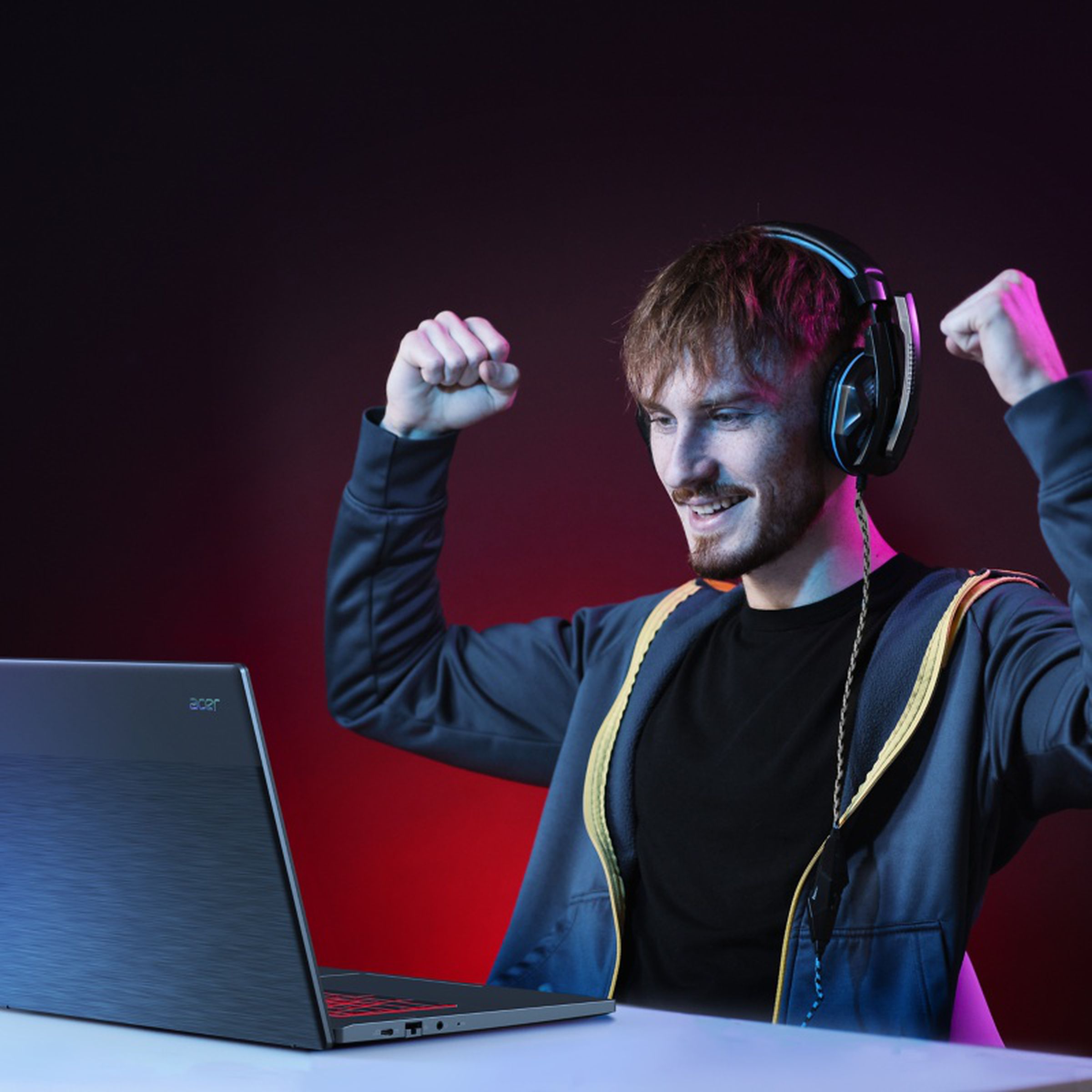 A user, wearing headphones, celebrates in front of an Acer gaming Chromebook in a dimly lit space.