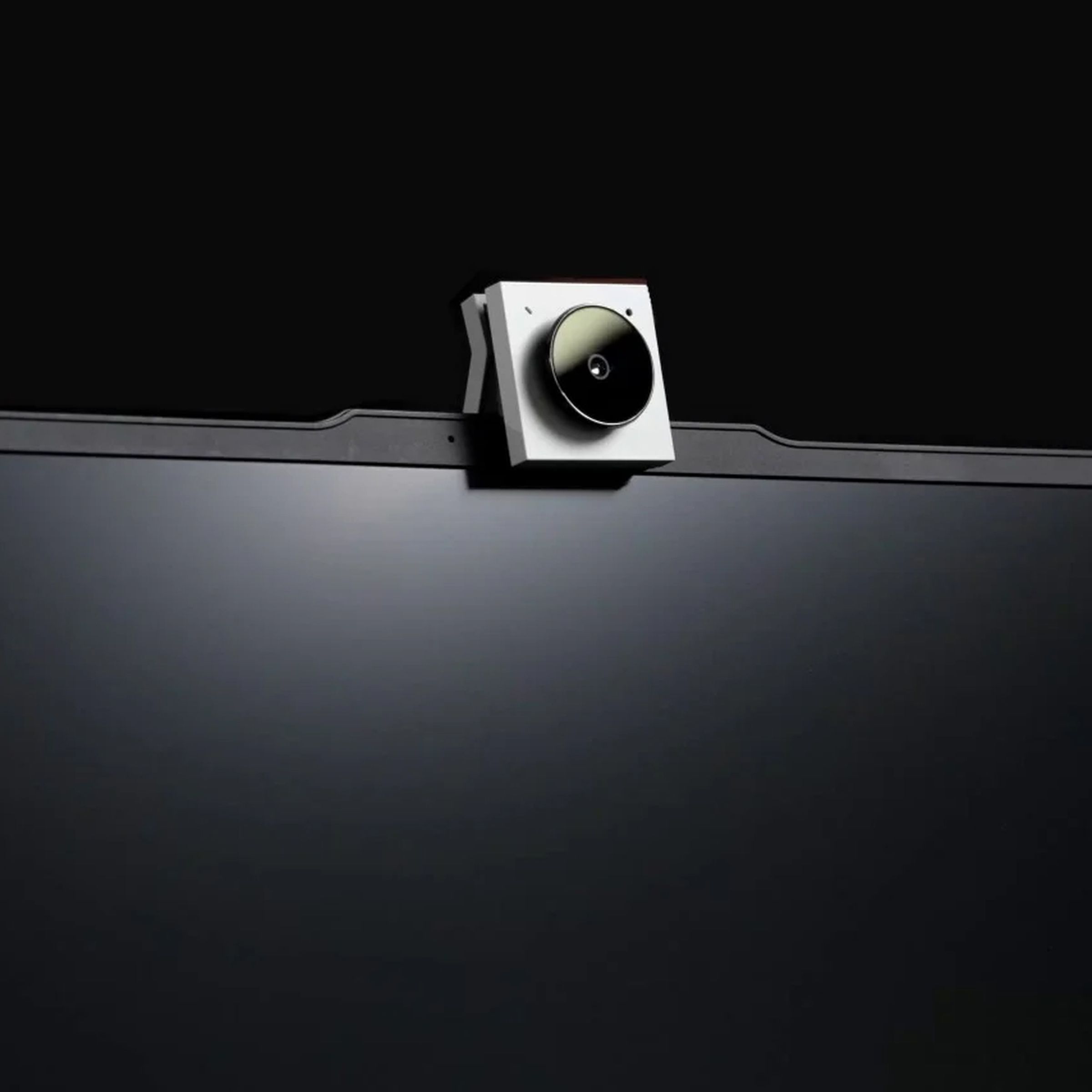 A white Opal Tadpole webcam sitting atop a black laptop against a black background.