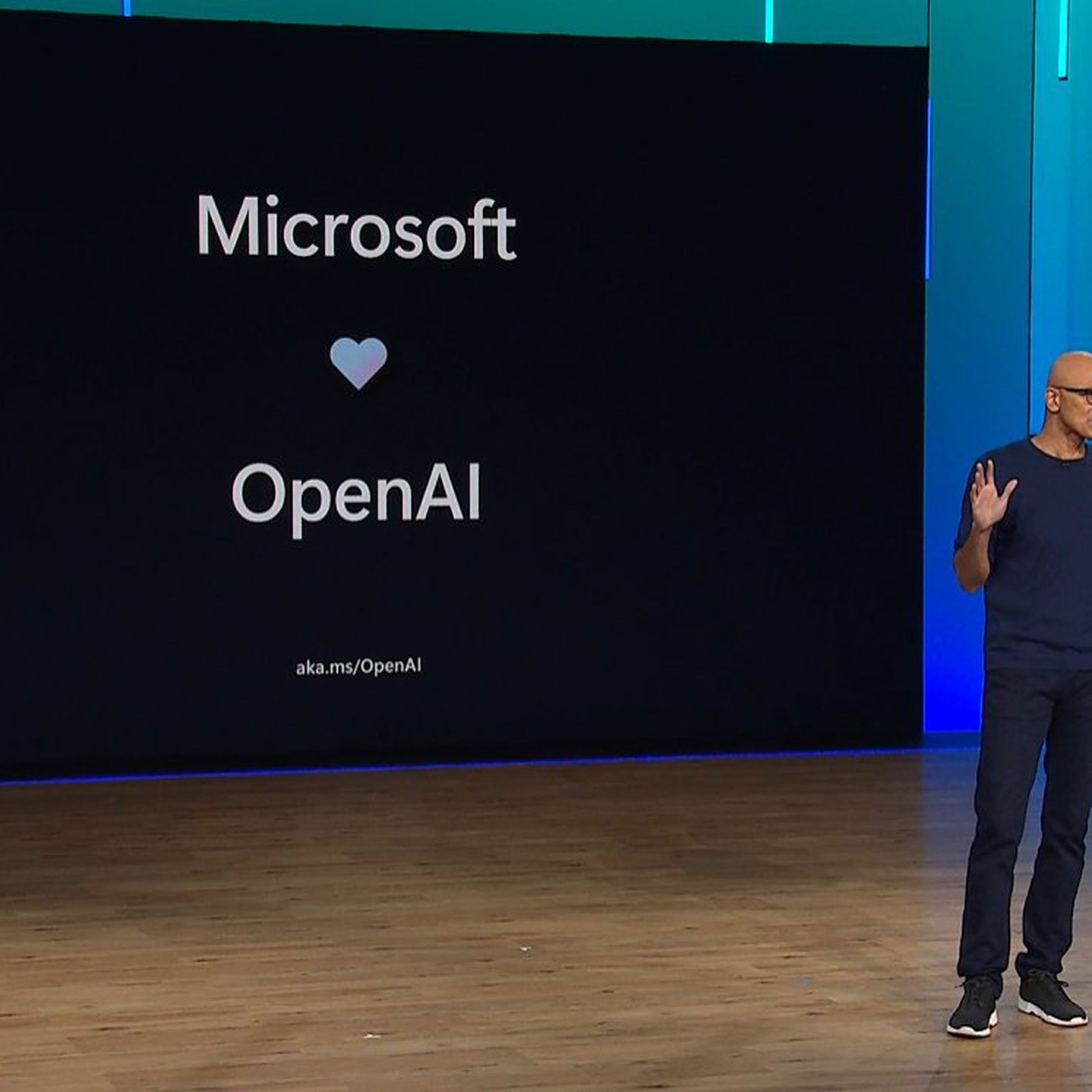 Photo of Satya Nadella standing in front of a sign that reads Microsoft loves OpenAI