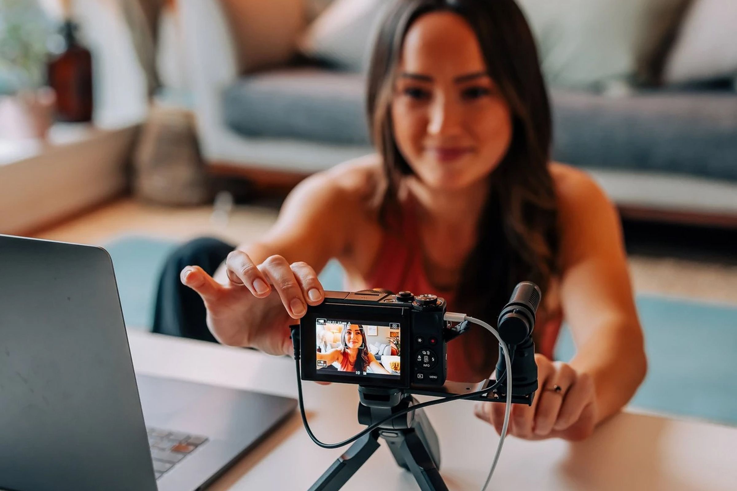 A person setting up a livestream of themselves at home with a tripod-mounted camera connected to a laptop.