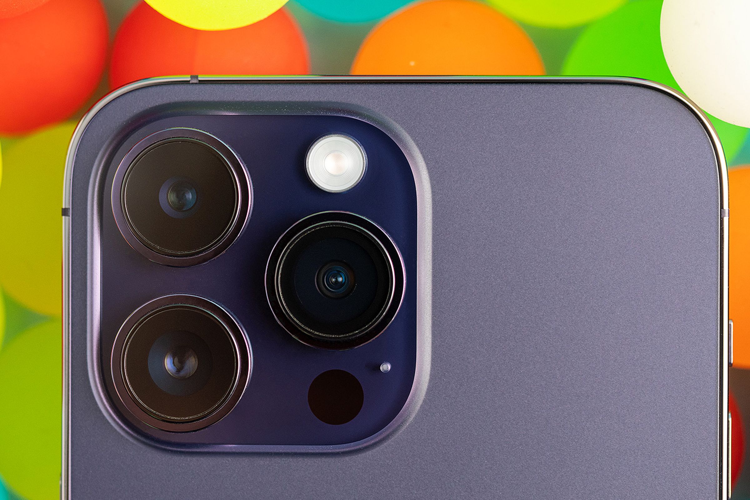 A close up image of the iPhone 14 Pro’s camera module on a background of translucent colorful balls.