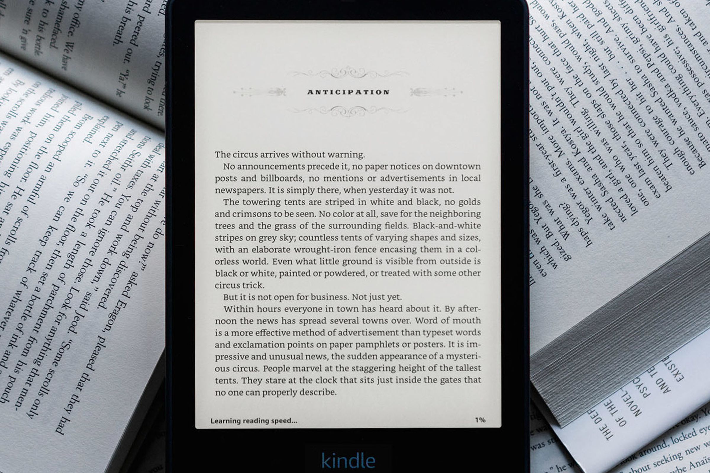 The Kindle Paperwhite e-reader turned on resting on a bunch of analog books.