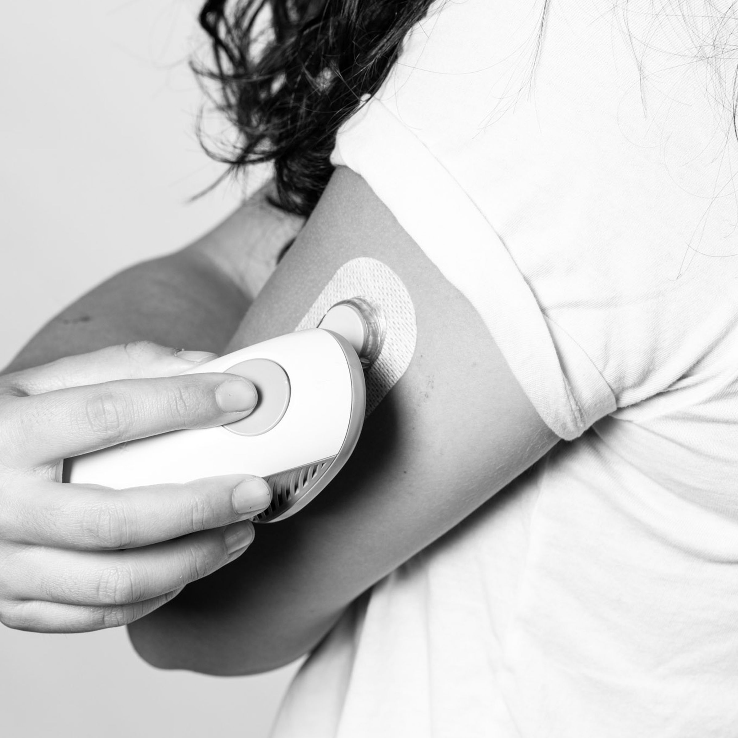 A black and white photo of Nicole Wetsman applying a Dexcom G6 transmitter to the back of her upper arm.