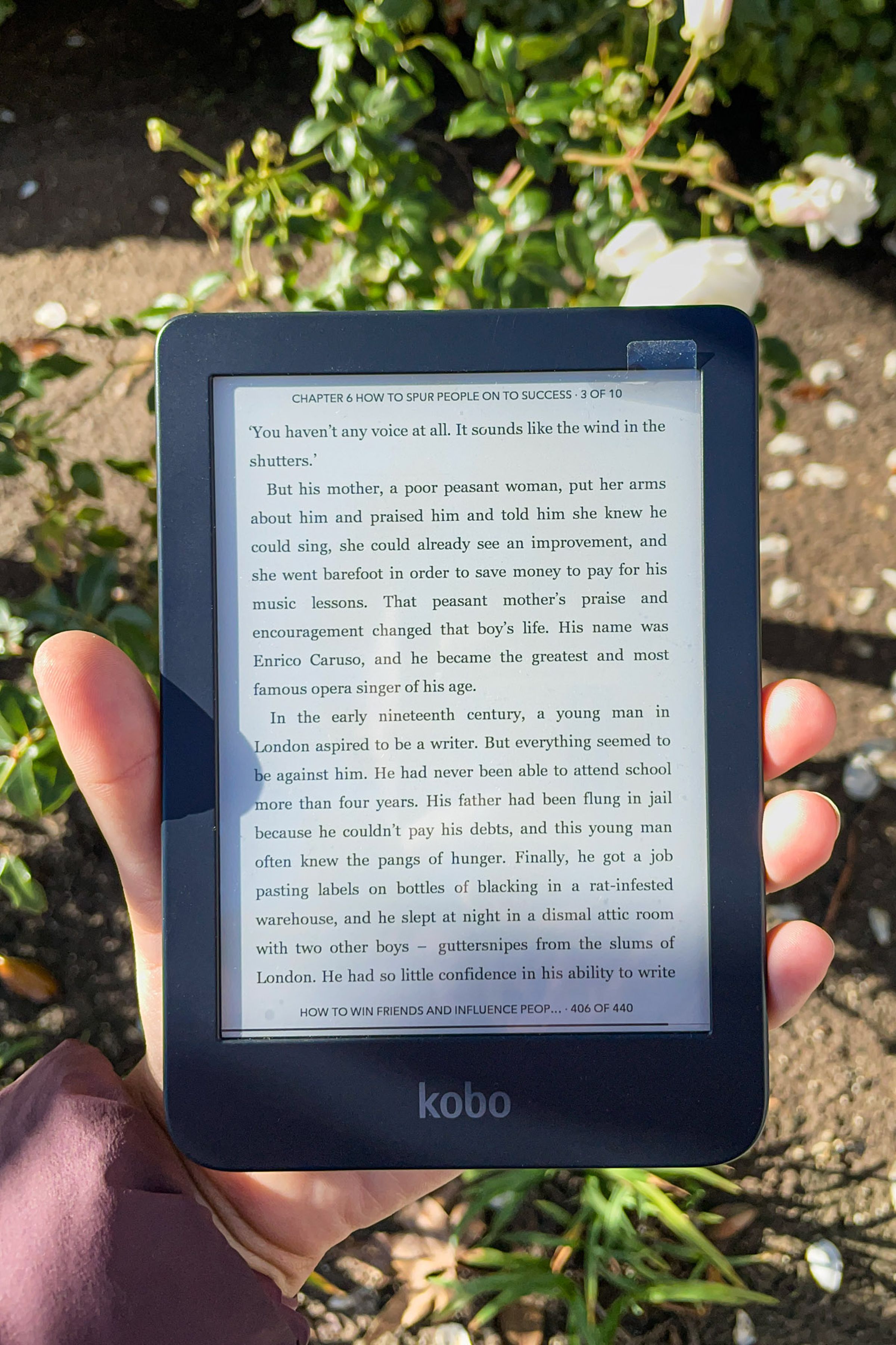 A hand holding up the Kobo Clara 2E. Its screen is on and open to a page in an ebook.