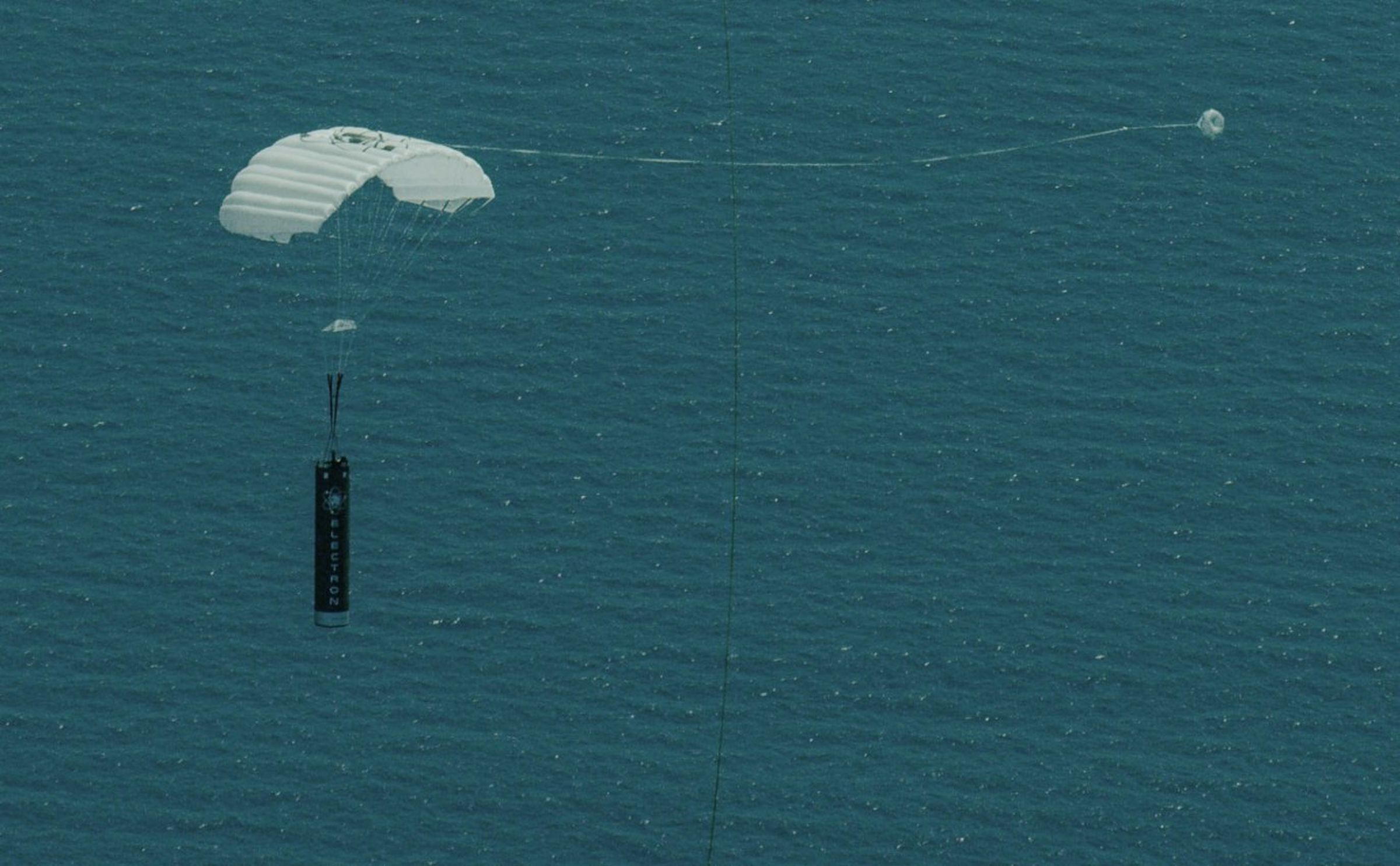 Rocket Lab’s Electron first stage floats under a parachute for a return splashdown test after launching satellites to space.