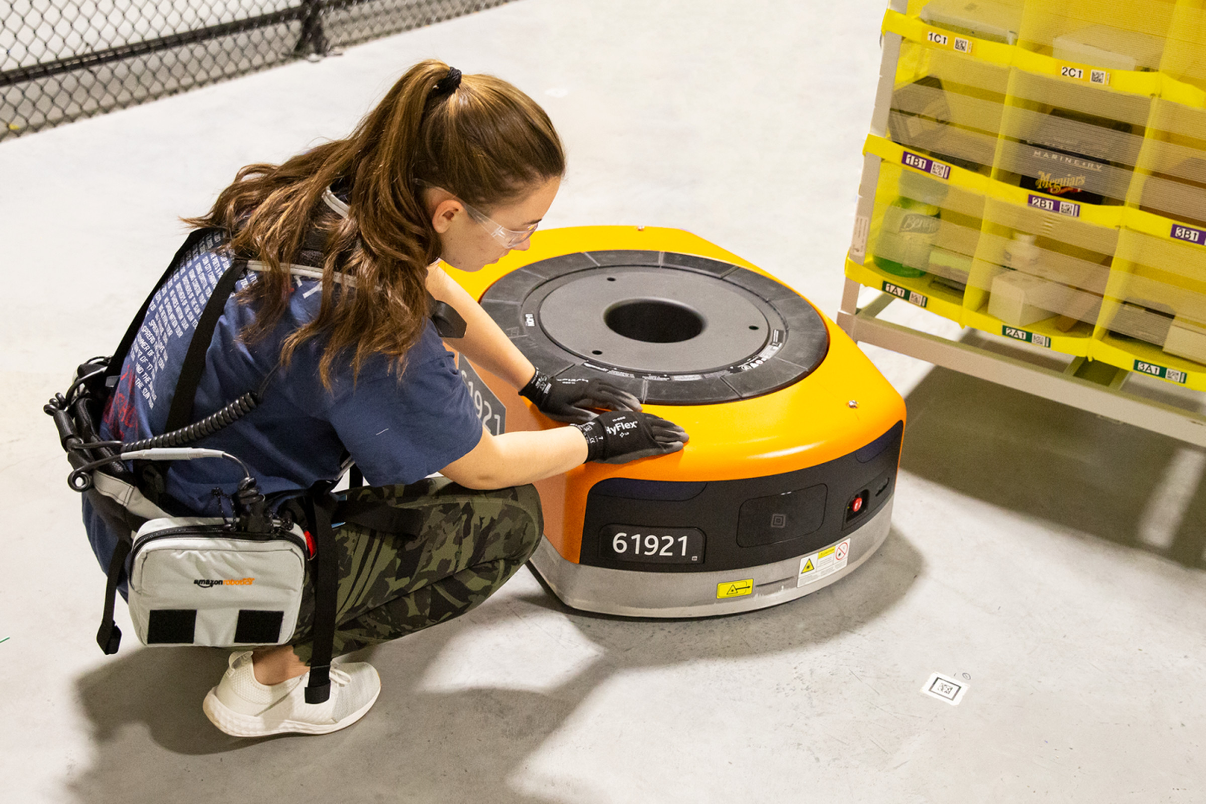 An Amazon employee wearing the Robotic Tech Vest inspects a warehouse robot. 