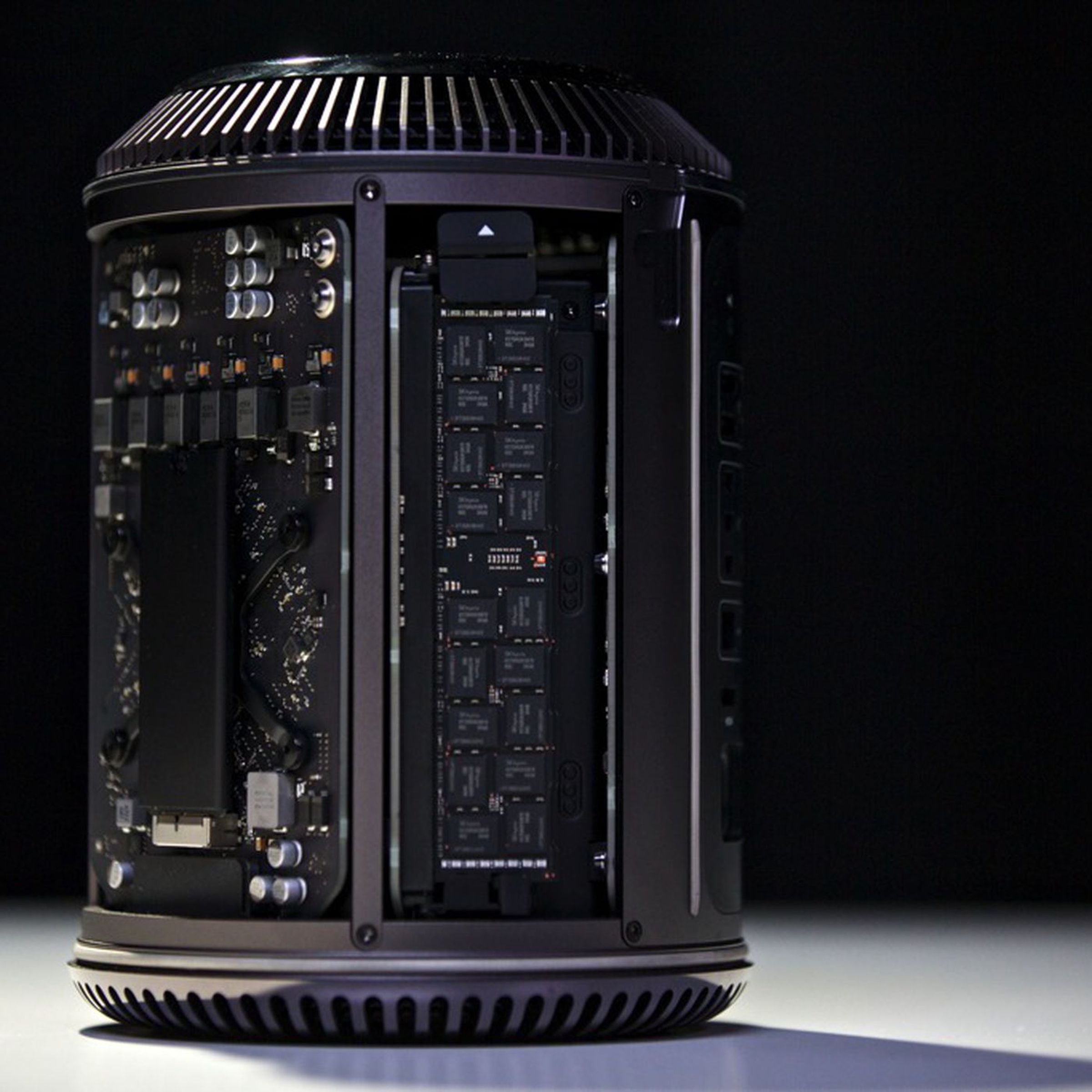 A picture of the 2013 Mac Pro sitting on a table without its cover, showing its innards, against a black background.