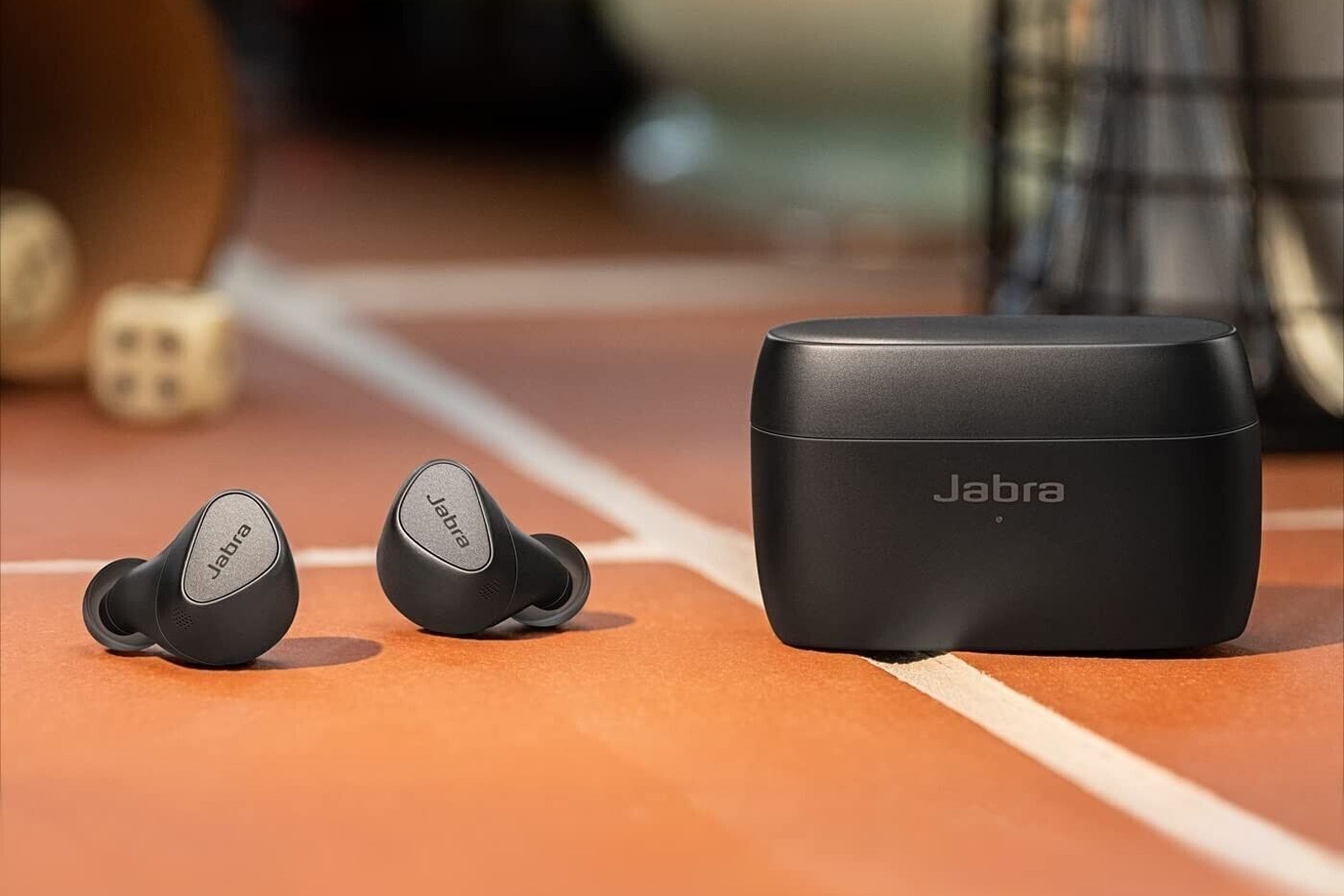 A black pair of the Jabra Elite 5 earbuds sitting beside their case on a red, tiled floor.