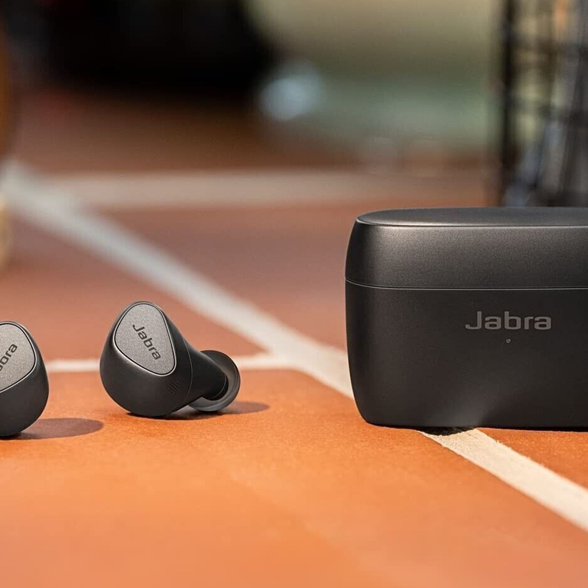 A black pair of the Jabra Elite 5 earbuds sitting beside their case on a red, tiled floor.