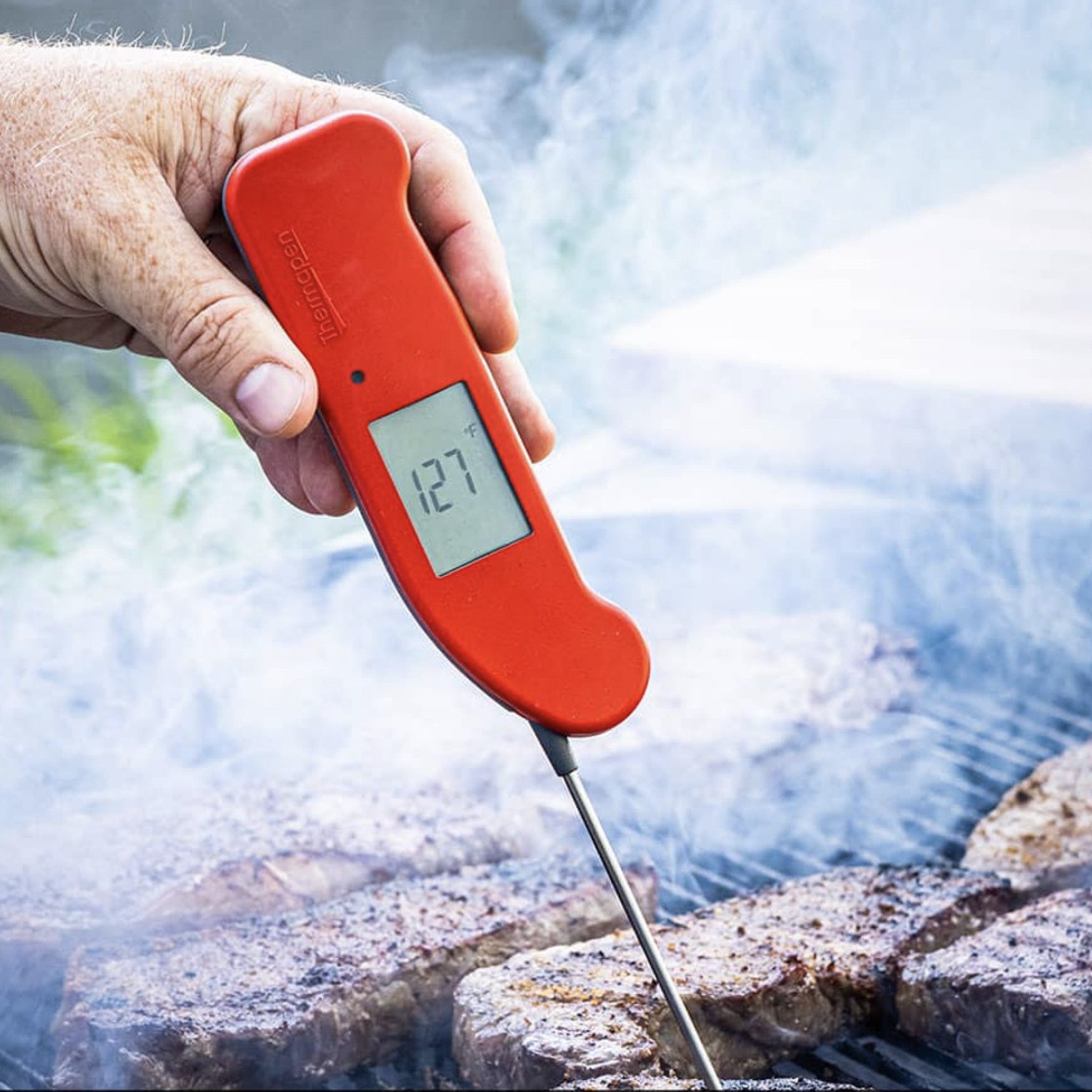 Hand holding Thermapen One thermometer into a grilled steak.