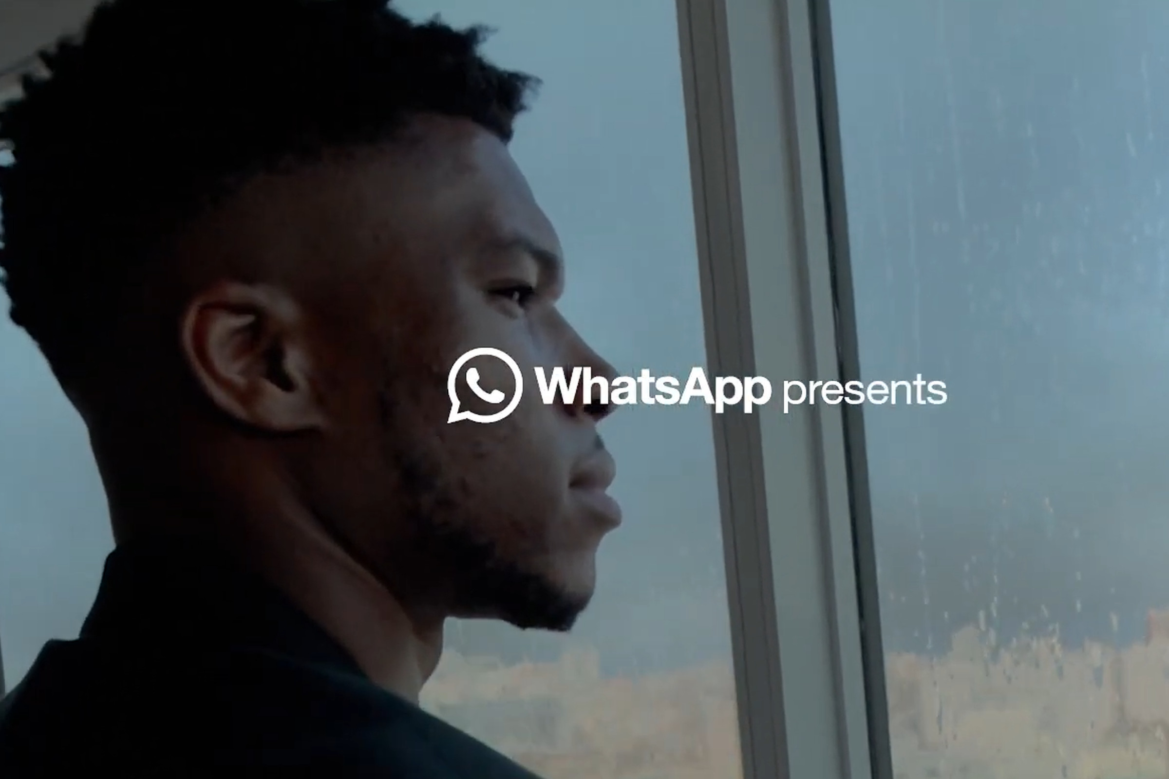 Giannis Antetokounmpo stands in front of a window. The WhatsApp logo is overlaid in front of his face.