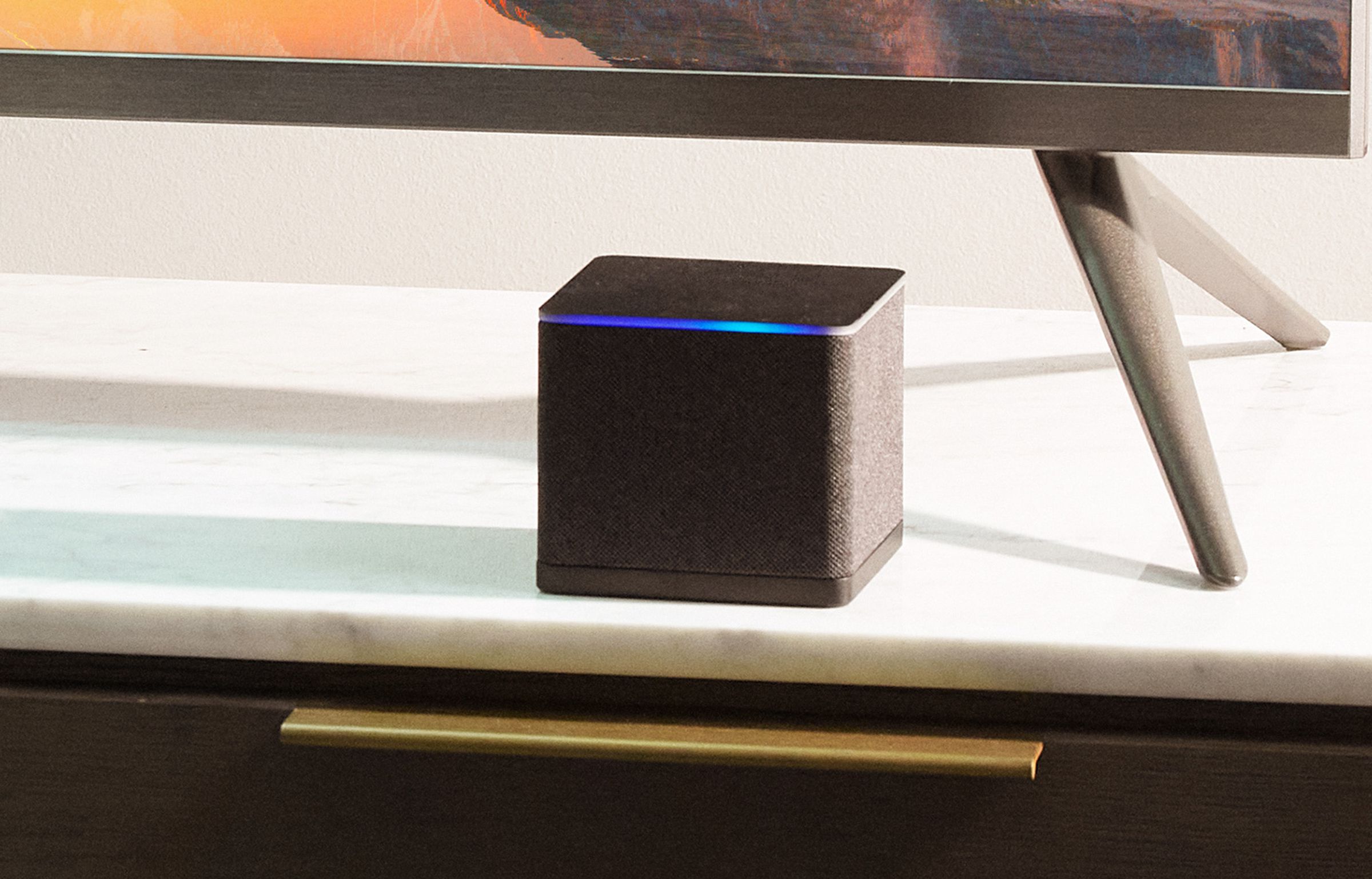 An image of the Amazon Fire TV Cube (2022) sitting below a television on a stand.