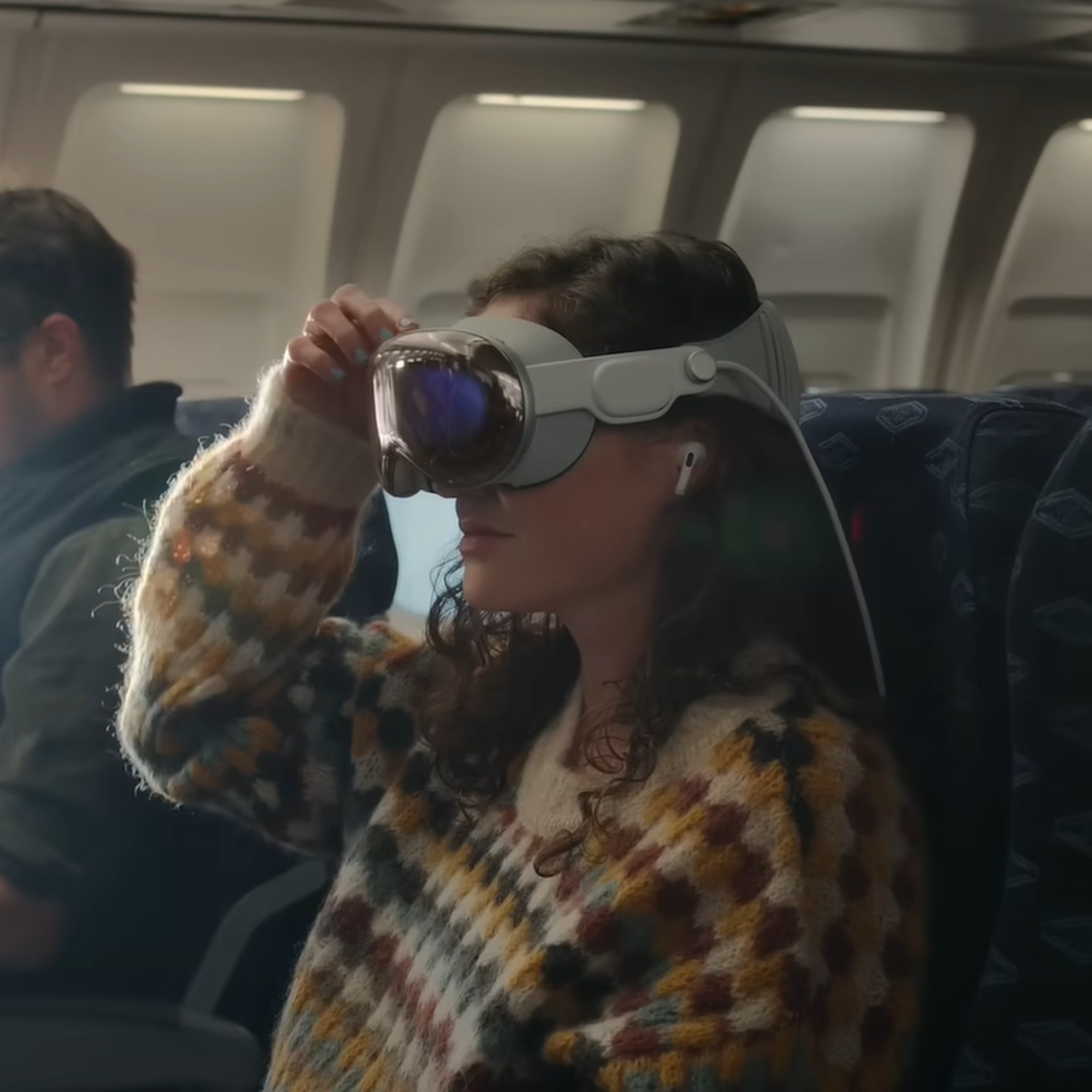 An image of a woman wearing Apple’s Vision Pro headset and AirPods Pro on a plane.