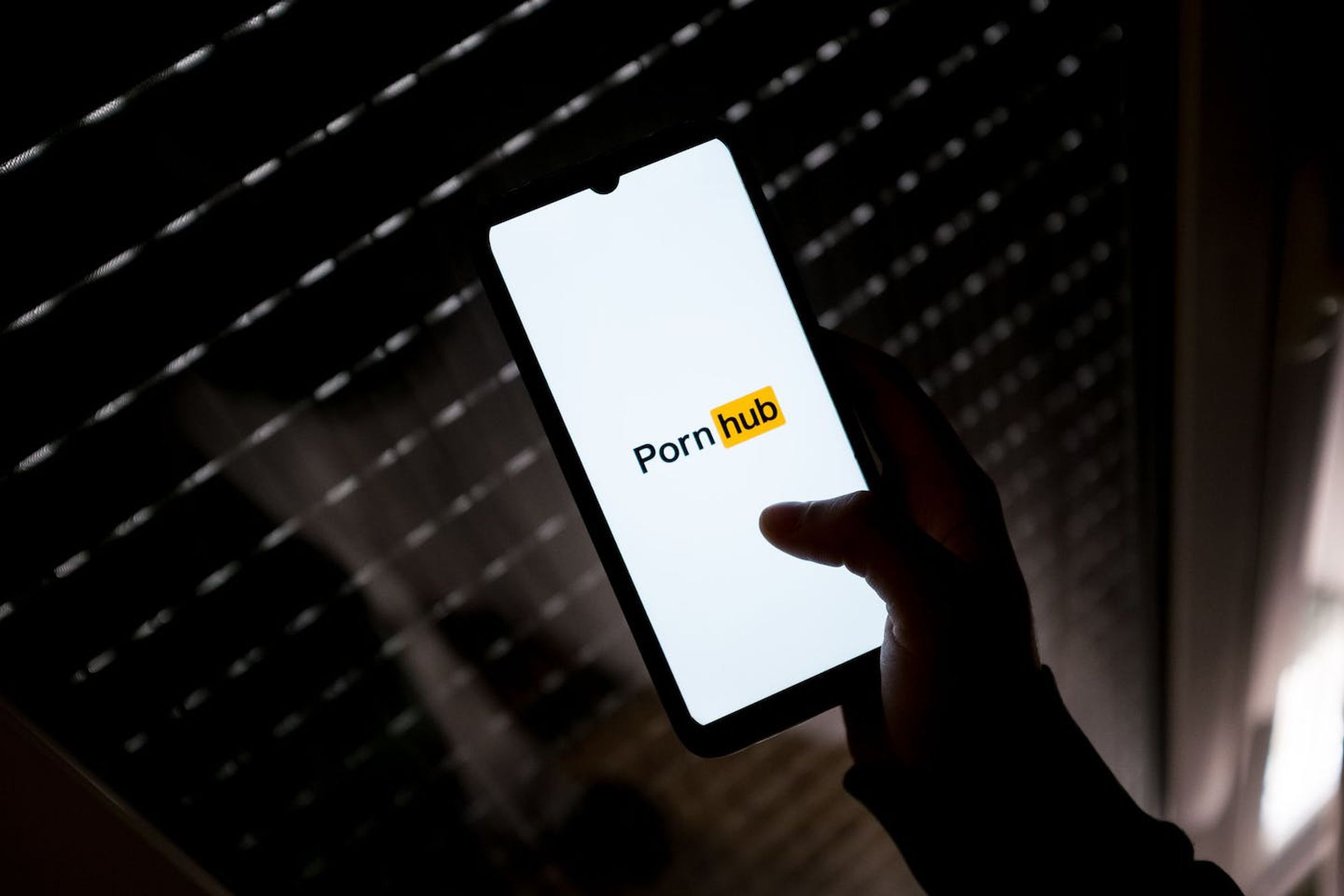 A hand holding up a smartphone with PornHub opened up in the dark.