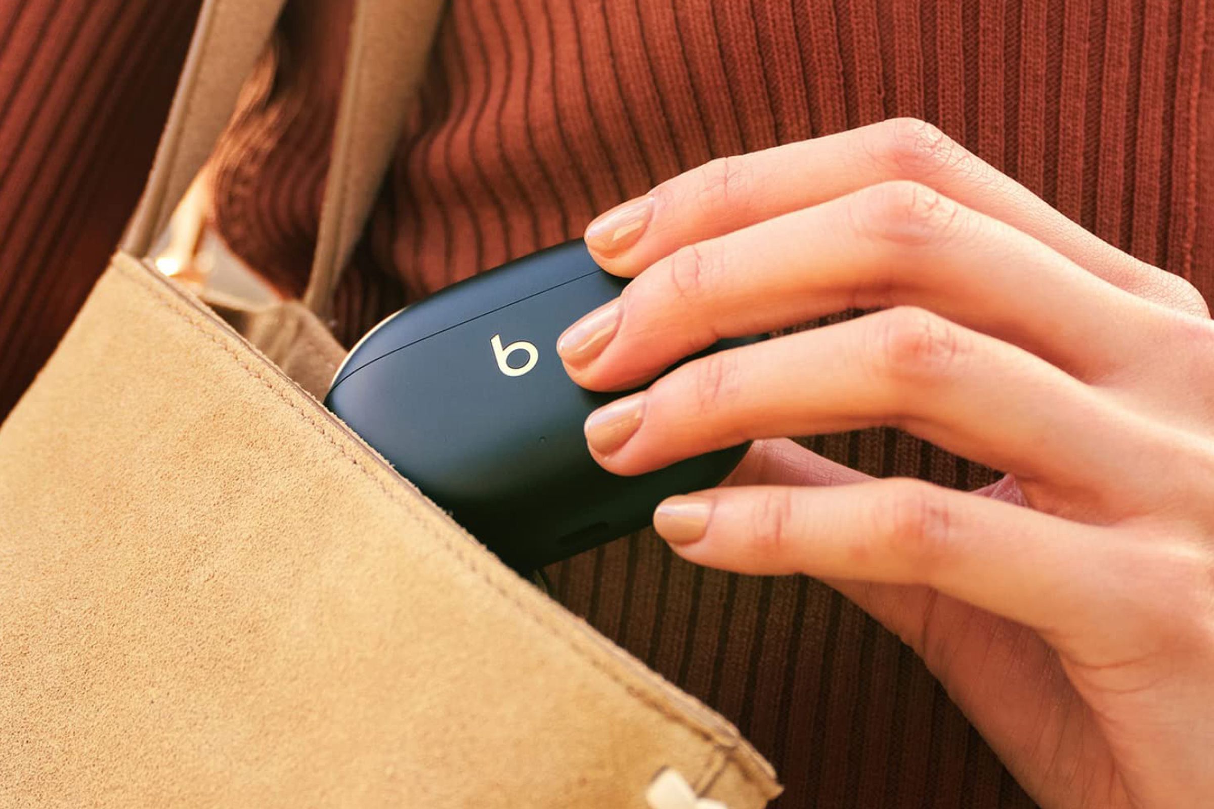 A close-up image of a hand pulling a pair of the Beats Studio Buds out of a purse.