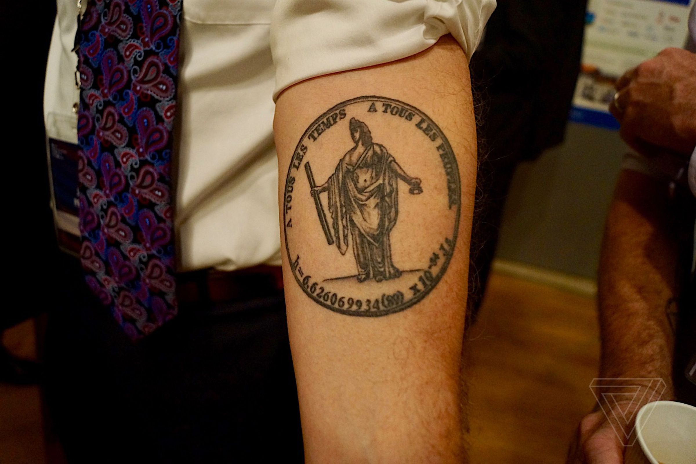 Jon Pratt, a physicist from NIST, shows off his metrology-themed tattoo. It shows the original seal of the BIPM (with a statue holding a prototype meter and kilogram), with Planck’s constant written underneath. 