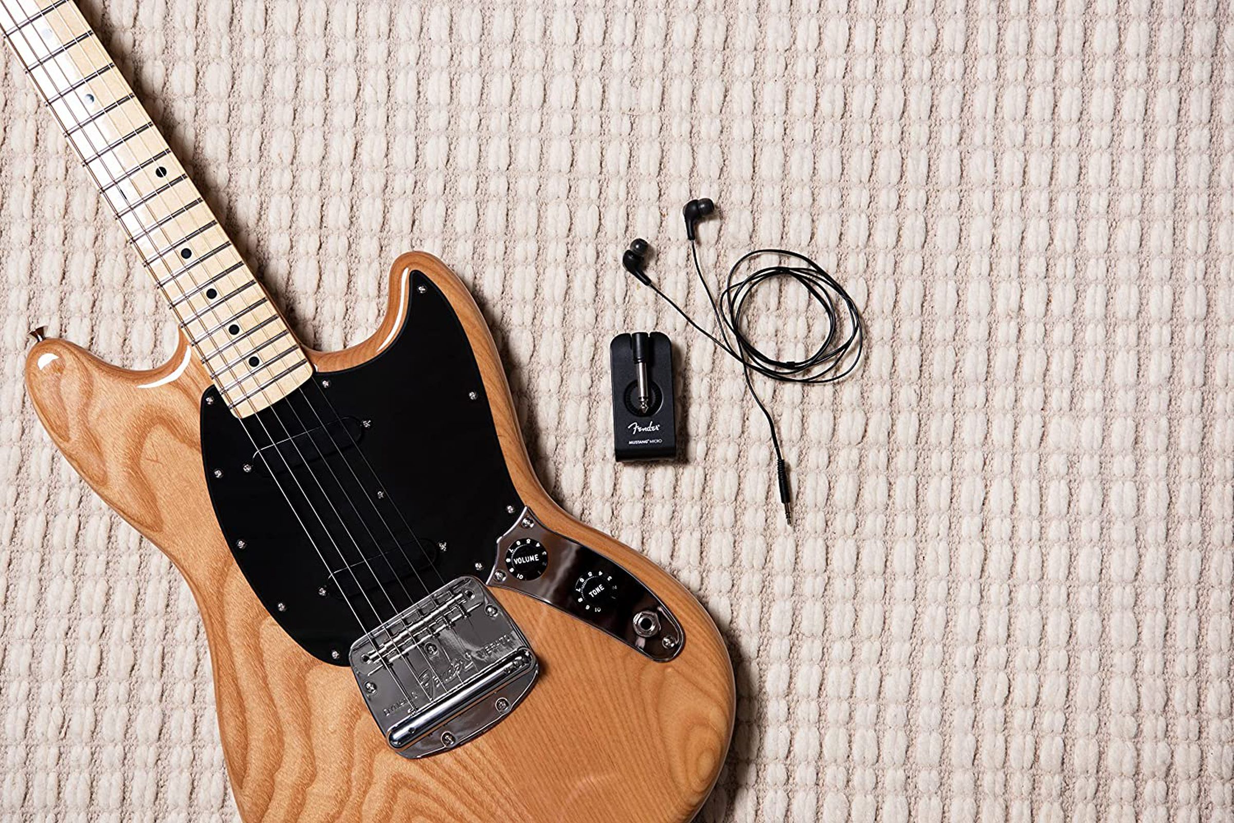 Small headphone amplifier to the left of an electric guitar.