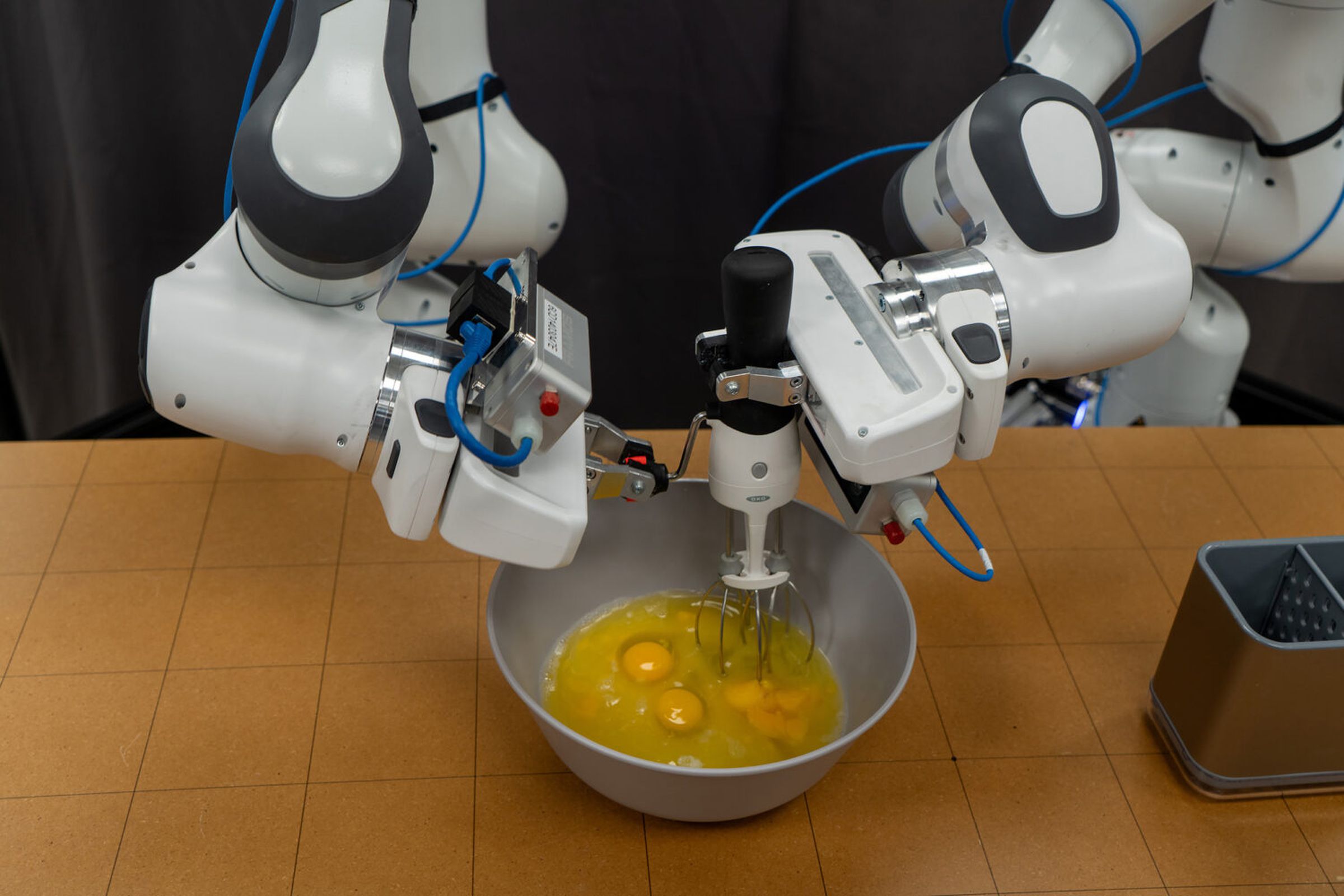 A picture of robotic arms whisking eggs in a metal bowl.